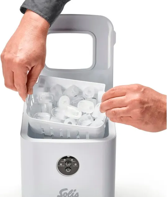 Mains retirant des glaçons d'une machine à glaçons blanche.