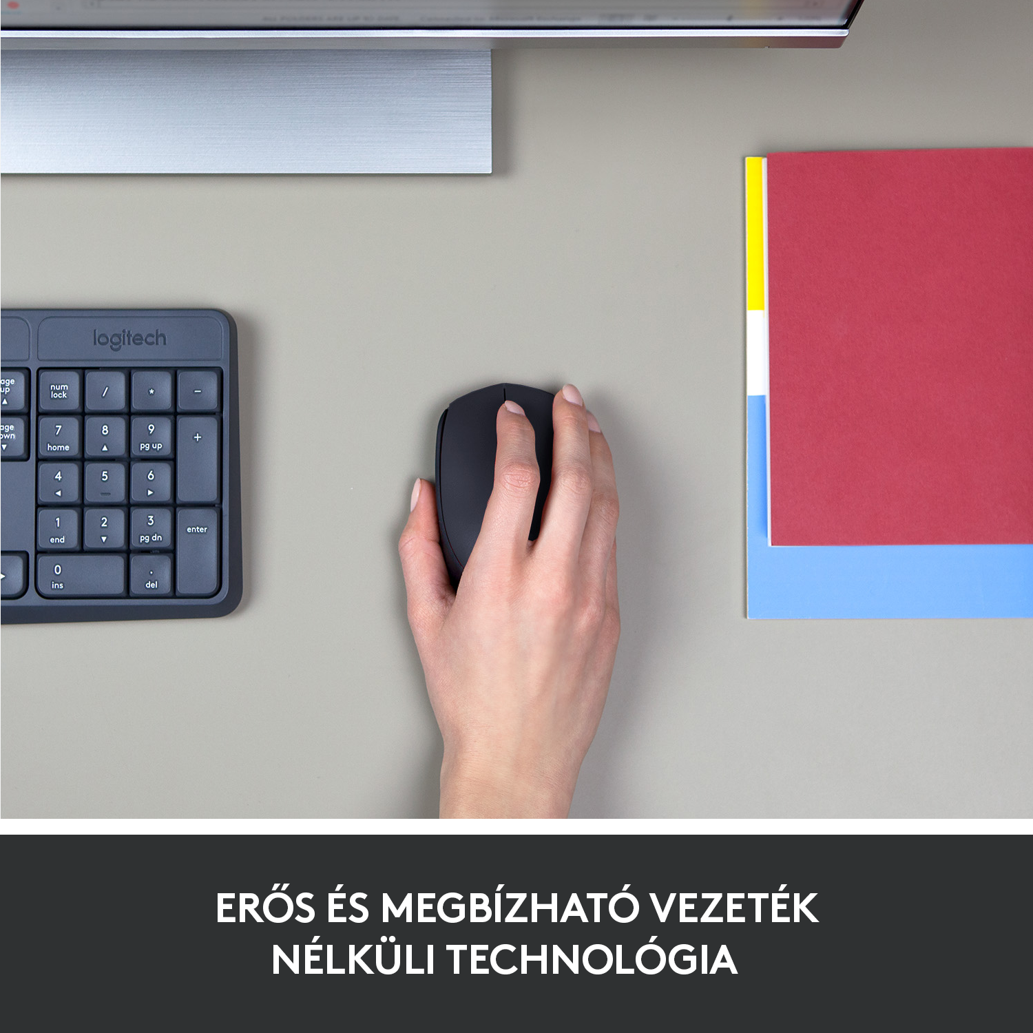 Egy kéz fekete egeret használ egy szürke felületen. Egy billentyűzet és papírok láthatók.
