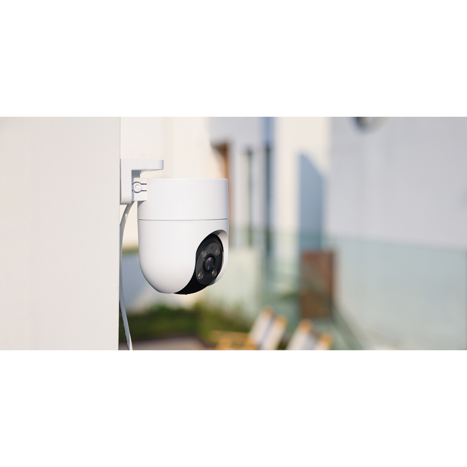 White security camera mounted on a wall. The lens is black, and the background is a building and sky.