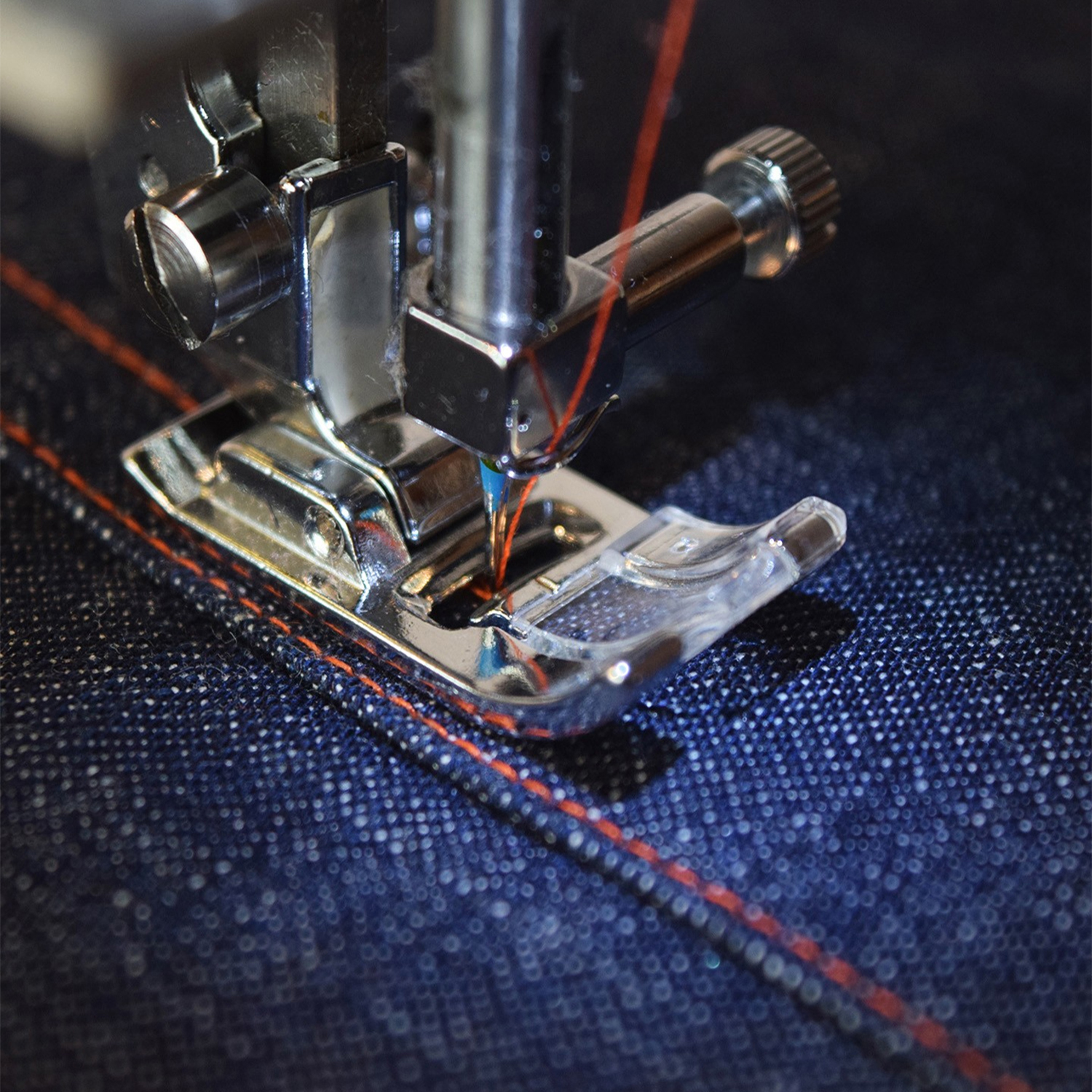 Primo piano di un ago di una macchina da cucire che cuce filo rosso in tessuto denim.