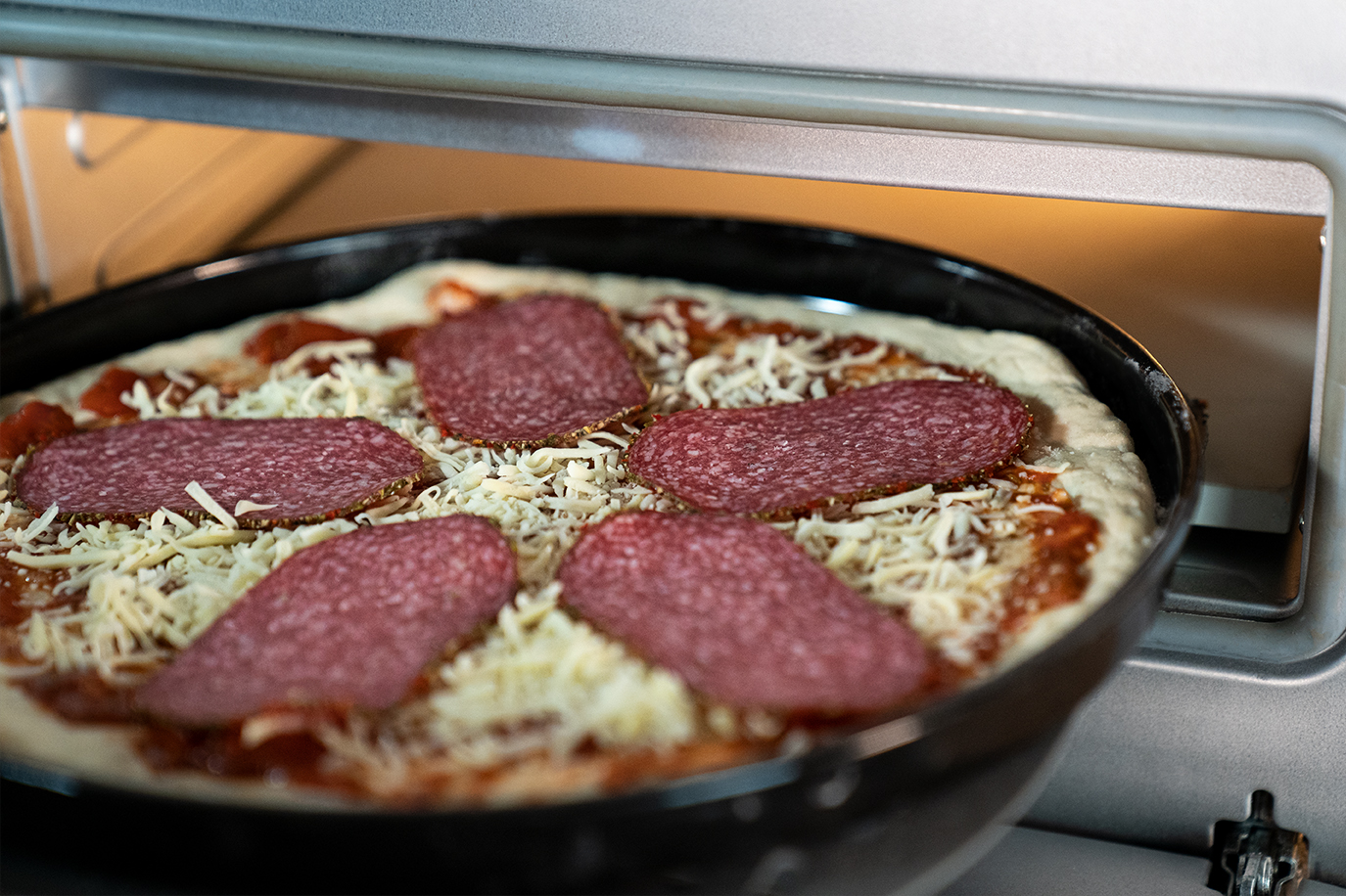 Pizza in einem Ofen. Salami-Scheiben und Käse sind auf der Pizza sichtbar.