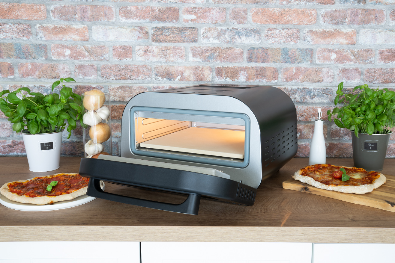 Ein offener Pizzaofen mit zwei Pizzen, einem Holzbrett und Basilikumpflanzen auf einem Holztisch.