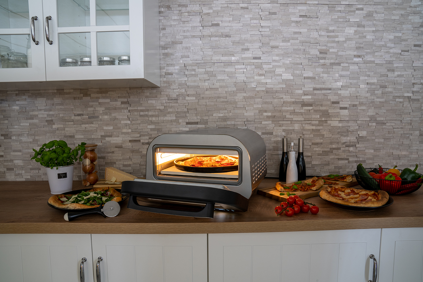 Ein Pizzaofen mit einer Pizza darin. Andere Pizzen, Zutaten und Utensilien sind auf der Theke.