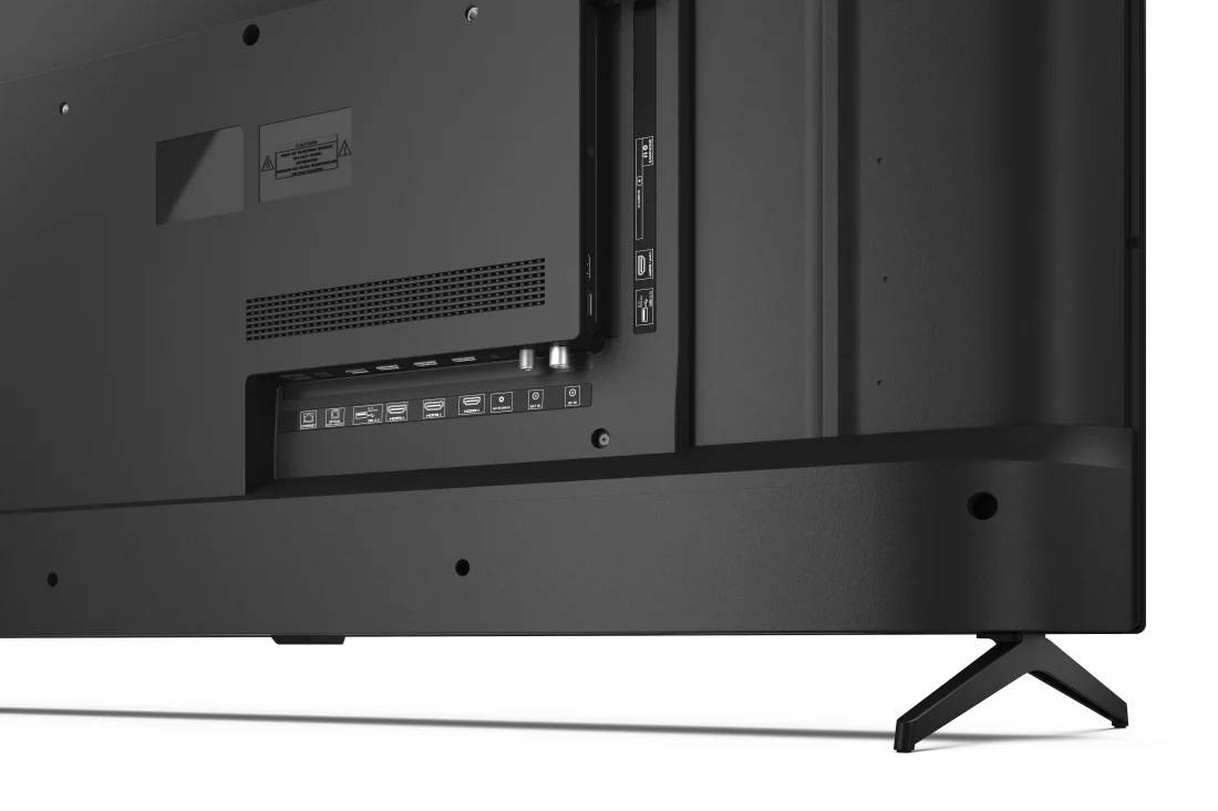 Parte trasera de un televisor negro con puertos. Incluye HDMI, USB y otros puertos. Soporte negro.