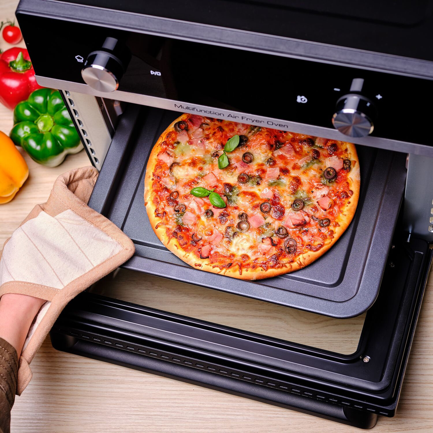 Pizza retirée d'un four friteuse à air multifonction. La pizza est sur un plateau, avec des feuilles de basilic.