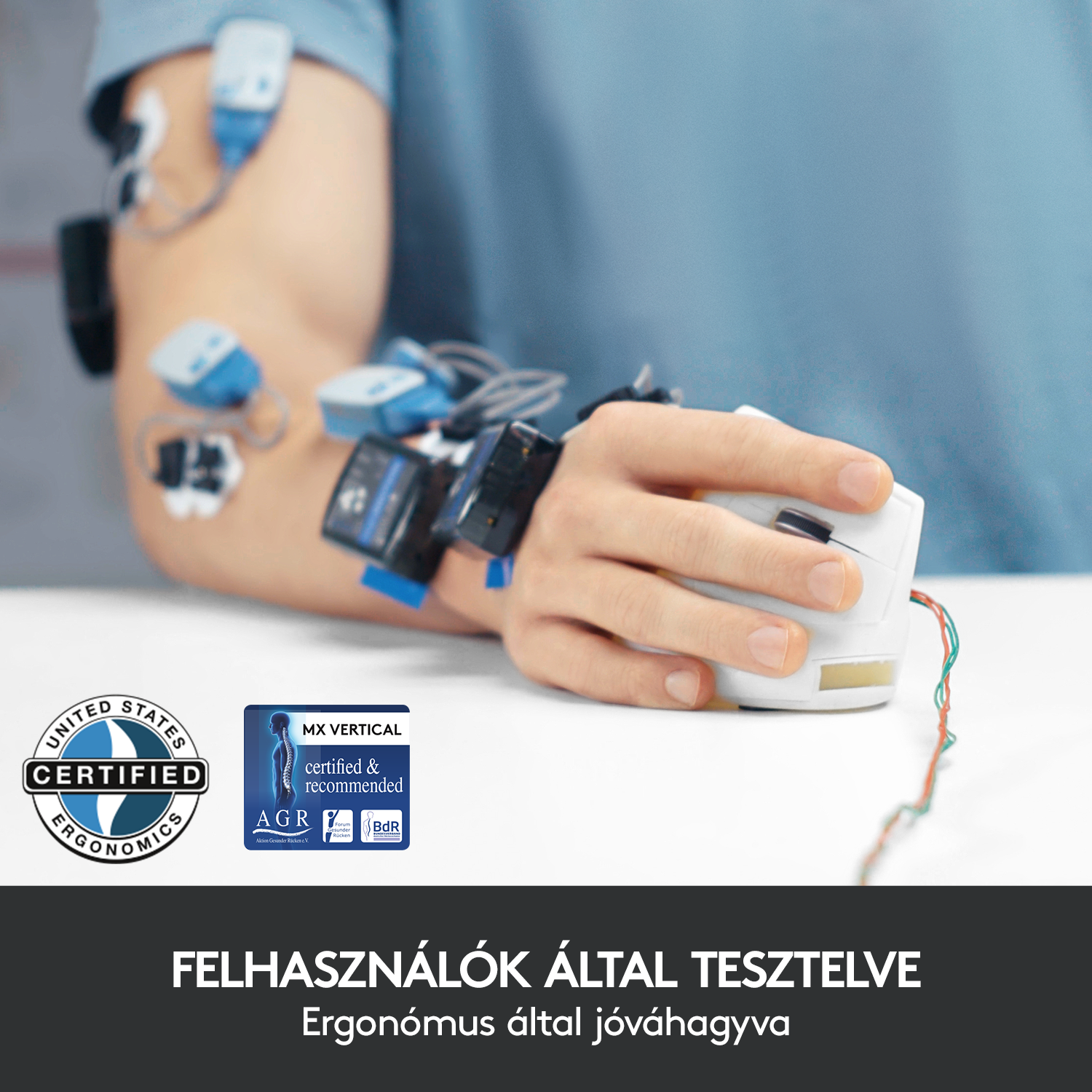 Egy személy keze, a csuklójához egy egér van rögzítve. Vezetékek és tapaszok vannak a karján.