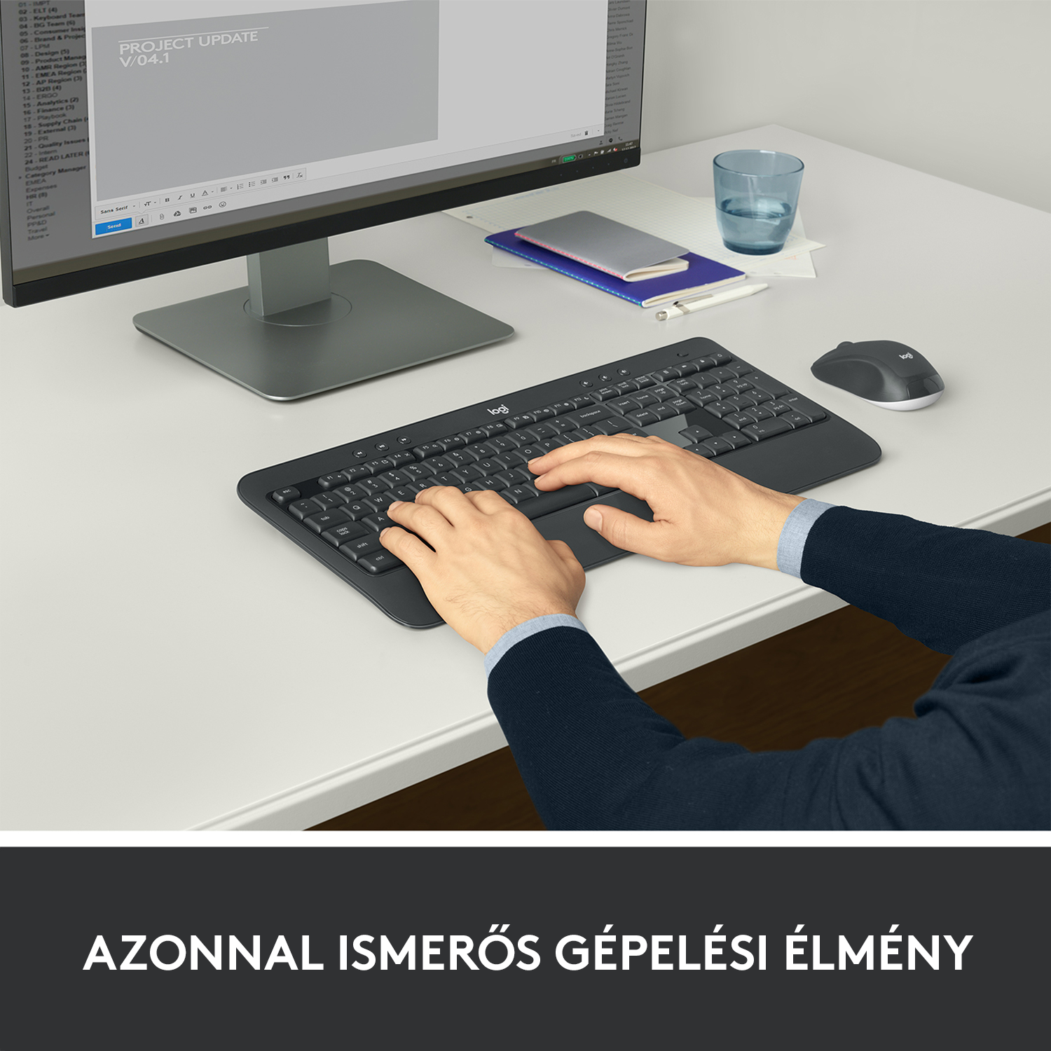 Kéz fekete billentyűzeten gépel, egér és monitor fehér asztalon.