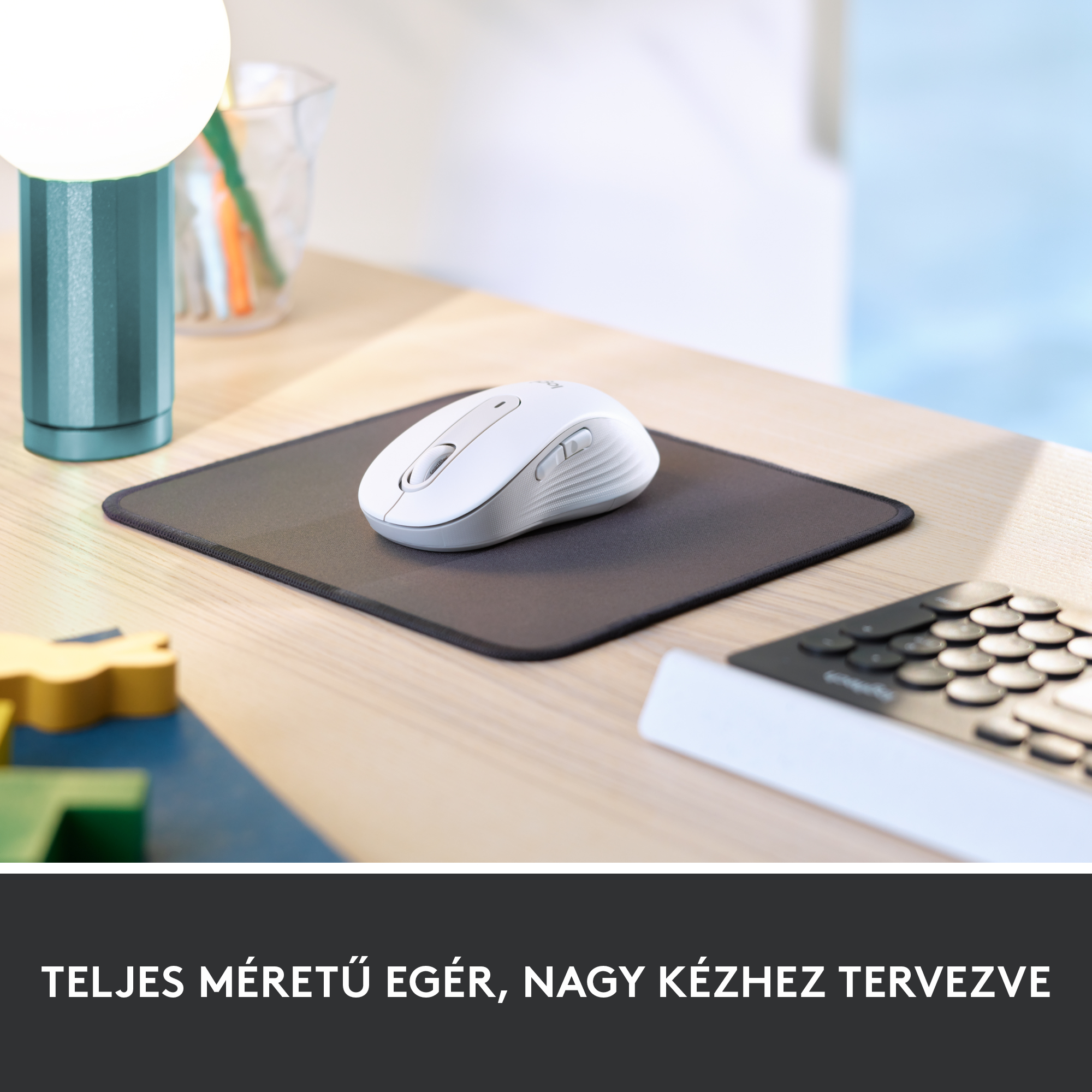 Fehér egér egy sötétszürke egéralátéten. Egy lámpa és más tárgyak egy fa asztalon.