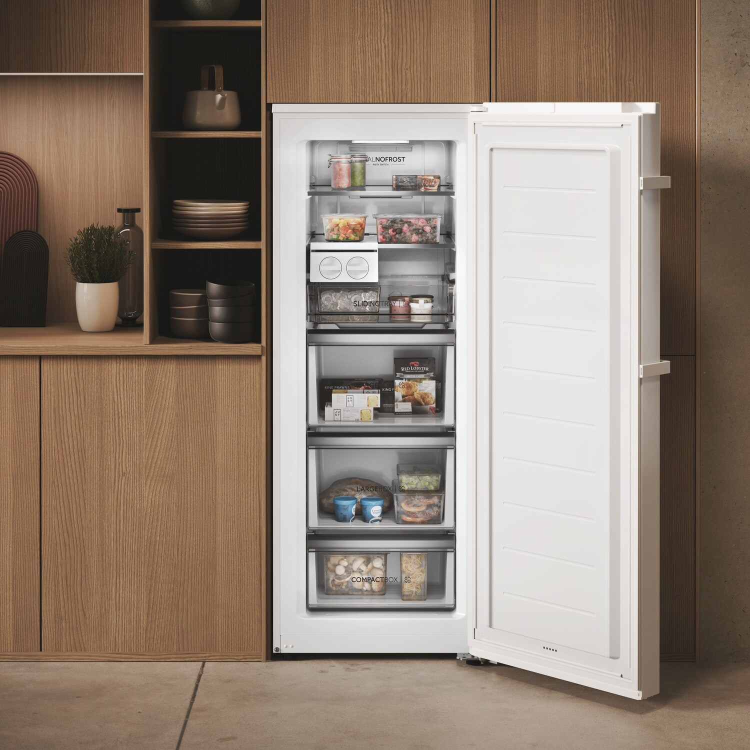 Réfrigérateur blanc avec porte ouverte, révélant des étagères avec des aliments. Des meubles en bois sont sur le côté.