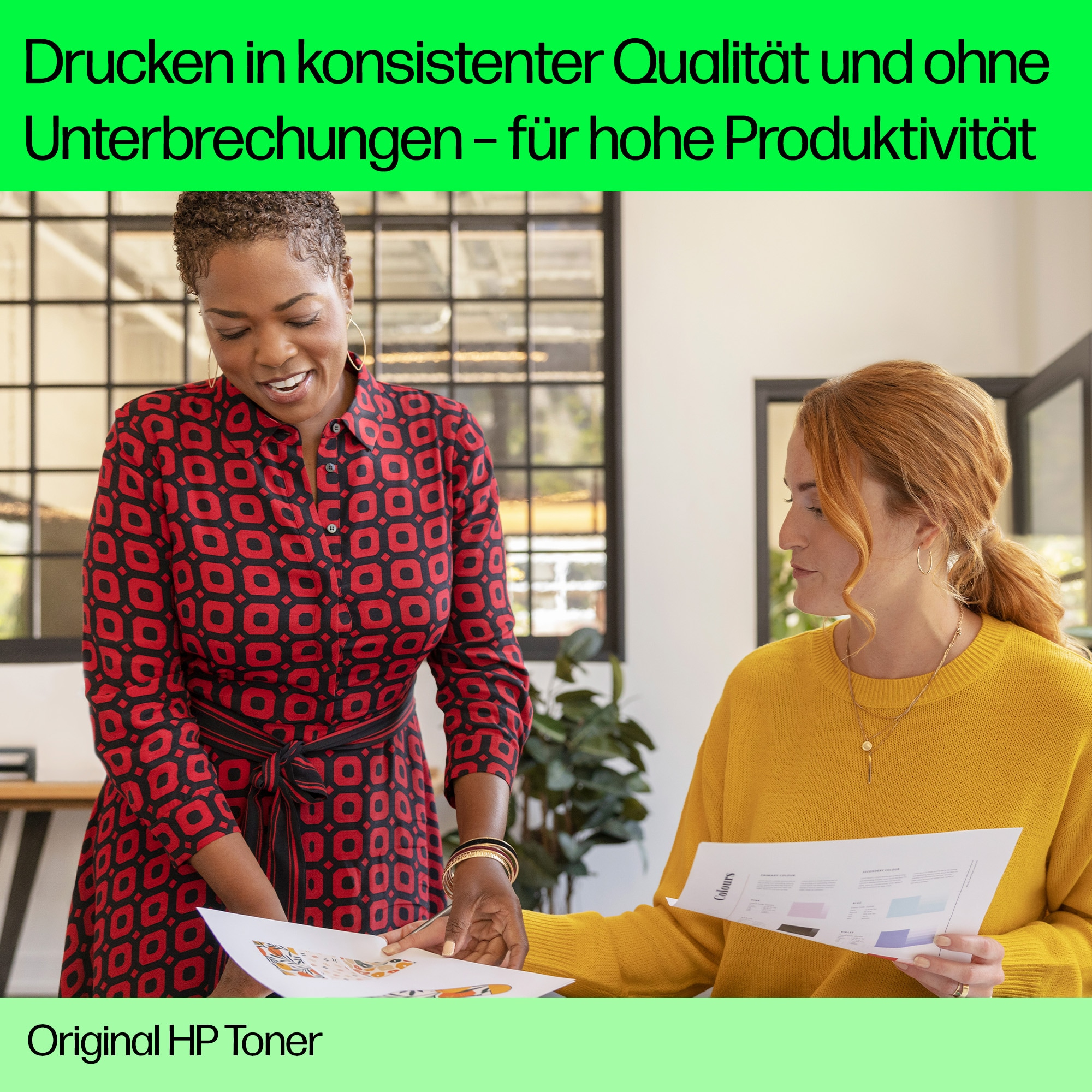 Zwei Frauen betrachten Papiere mit farbigen Grafiken. Eine trägt ein rotes Kleid.