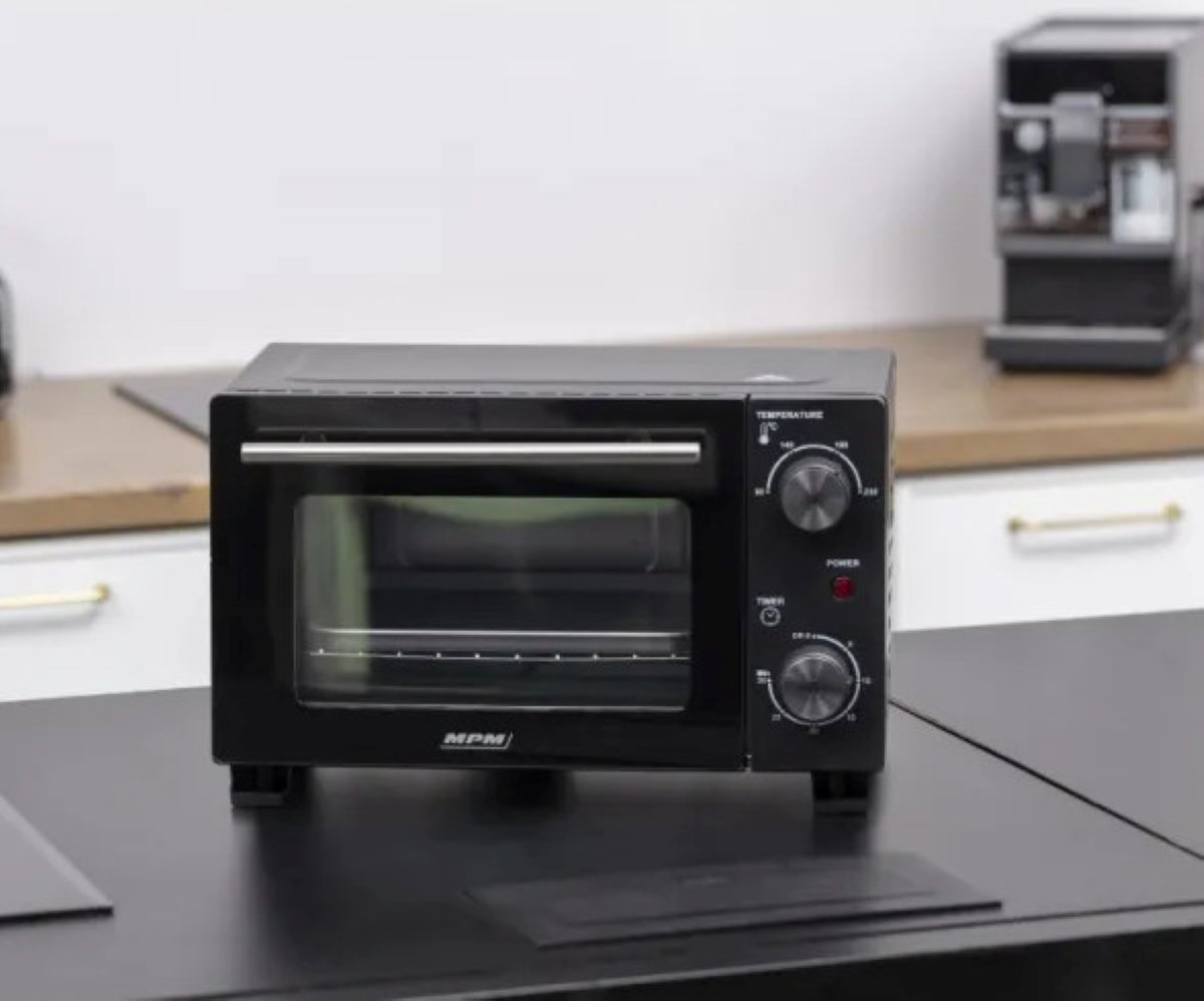 Czarny piekarnik na blacie z elementami sterującymi. Stoi na czarnym blacie, z ekspresem do kawy w tle.