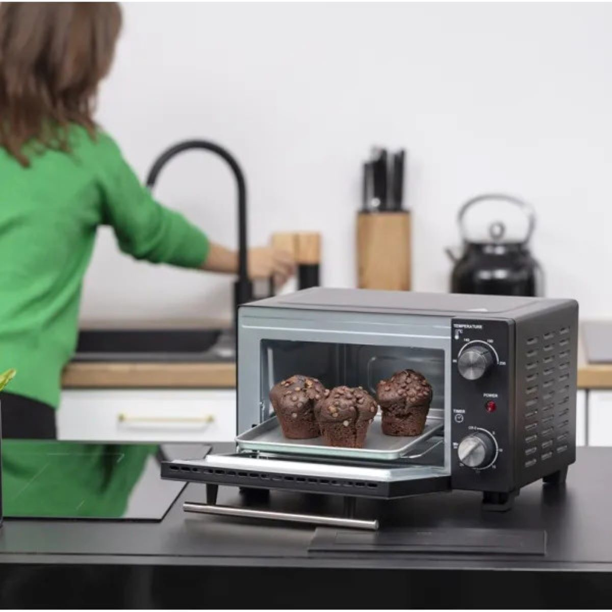 Czarny piekarnik z babeczkami. Osoba stoi w pobliżu. Piekarnik stoi na czarnym blacie.