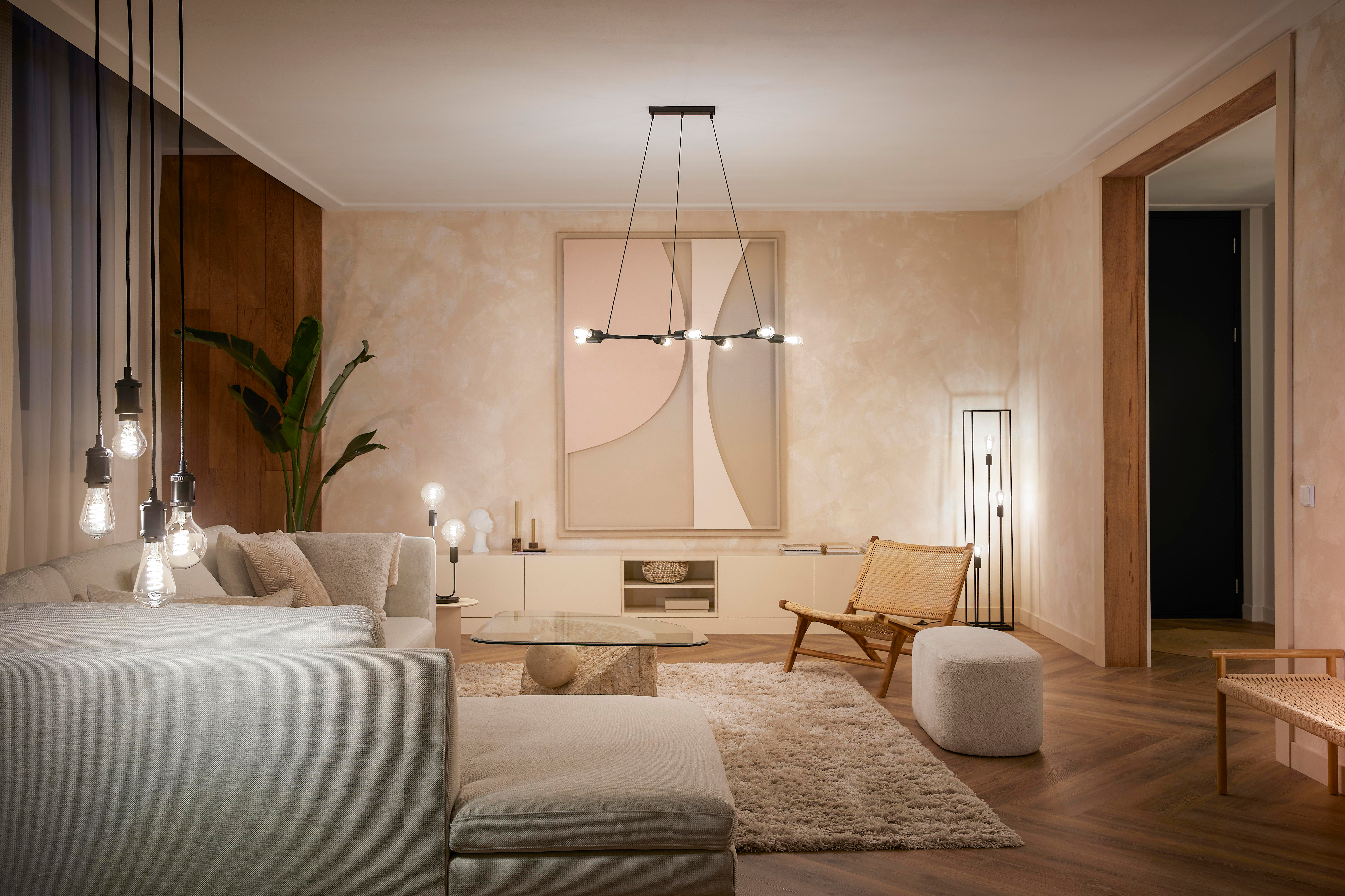 Wohnzimmer mit Sofa, Lampen, Kunst, Teppich und Holzboden. Warme Beleuchtung.