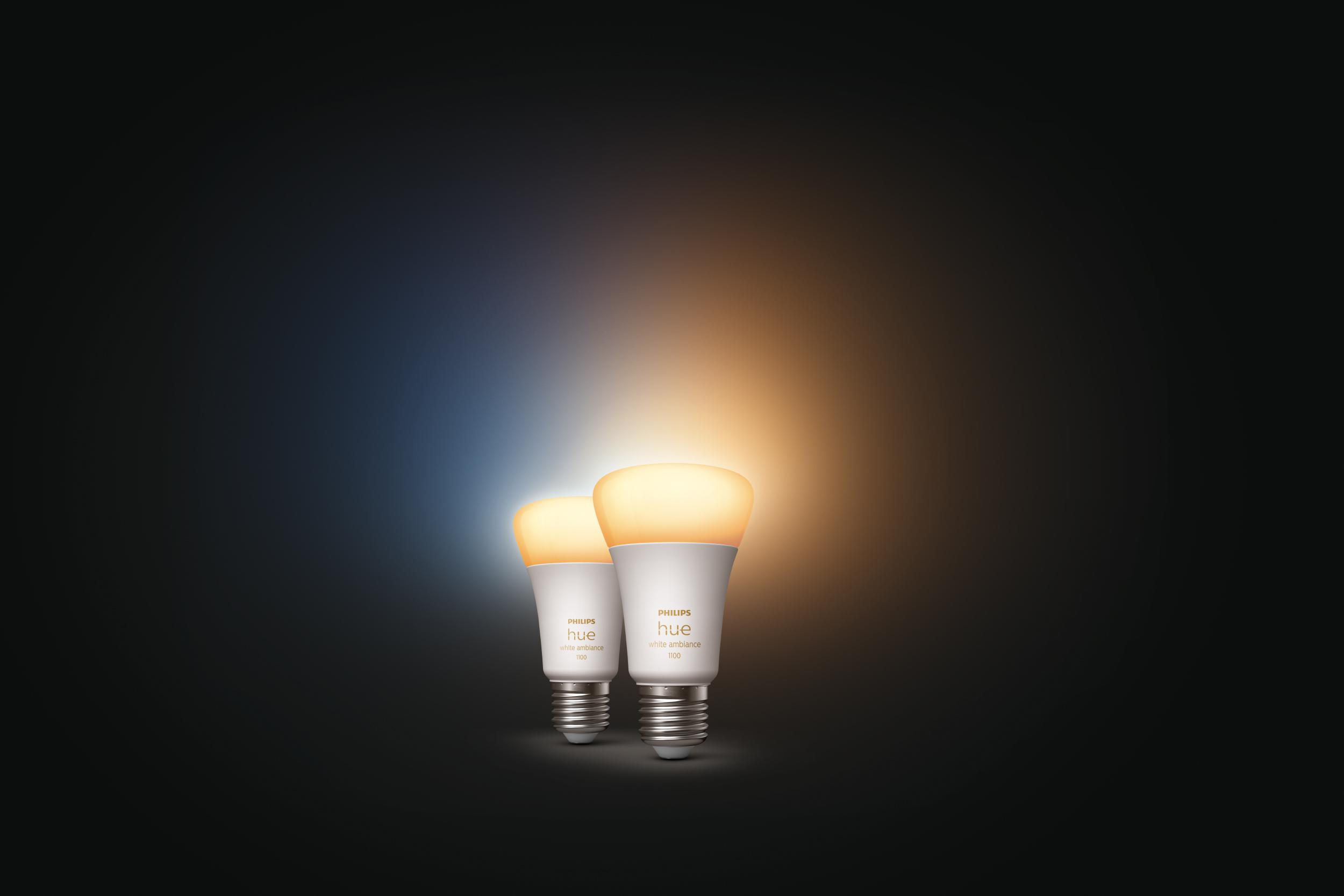 Zwei Philips Hue Smart-Glühbirnen mit warmweißem und kaltweißem Licht, vor dunklem Hintergrund.