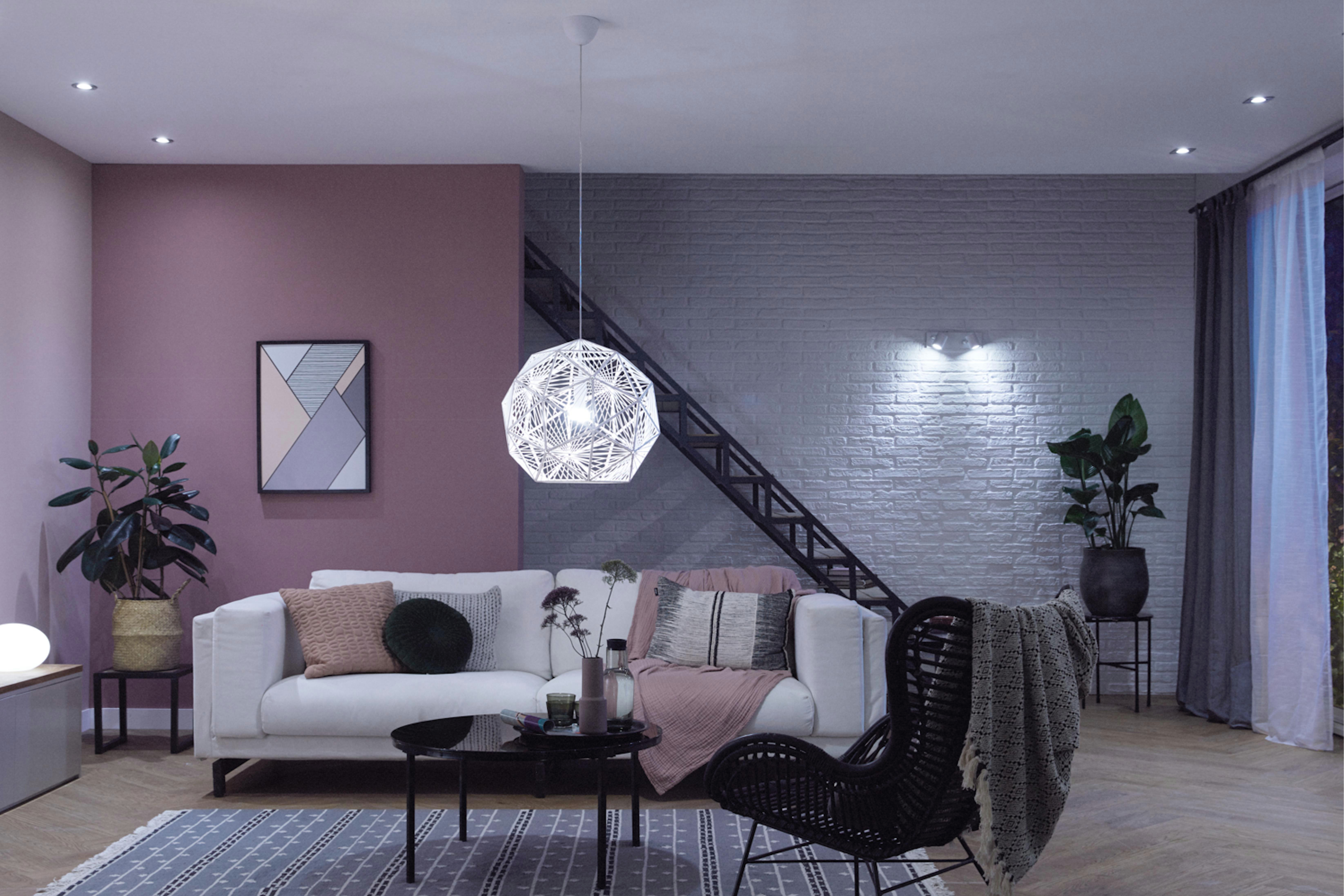 Wohnzimmer mit weißem Sofa, rosa Wand und dunkler Treppe, Pendelleuchte.