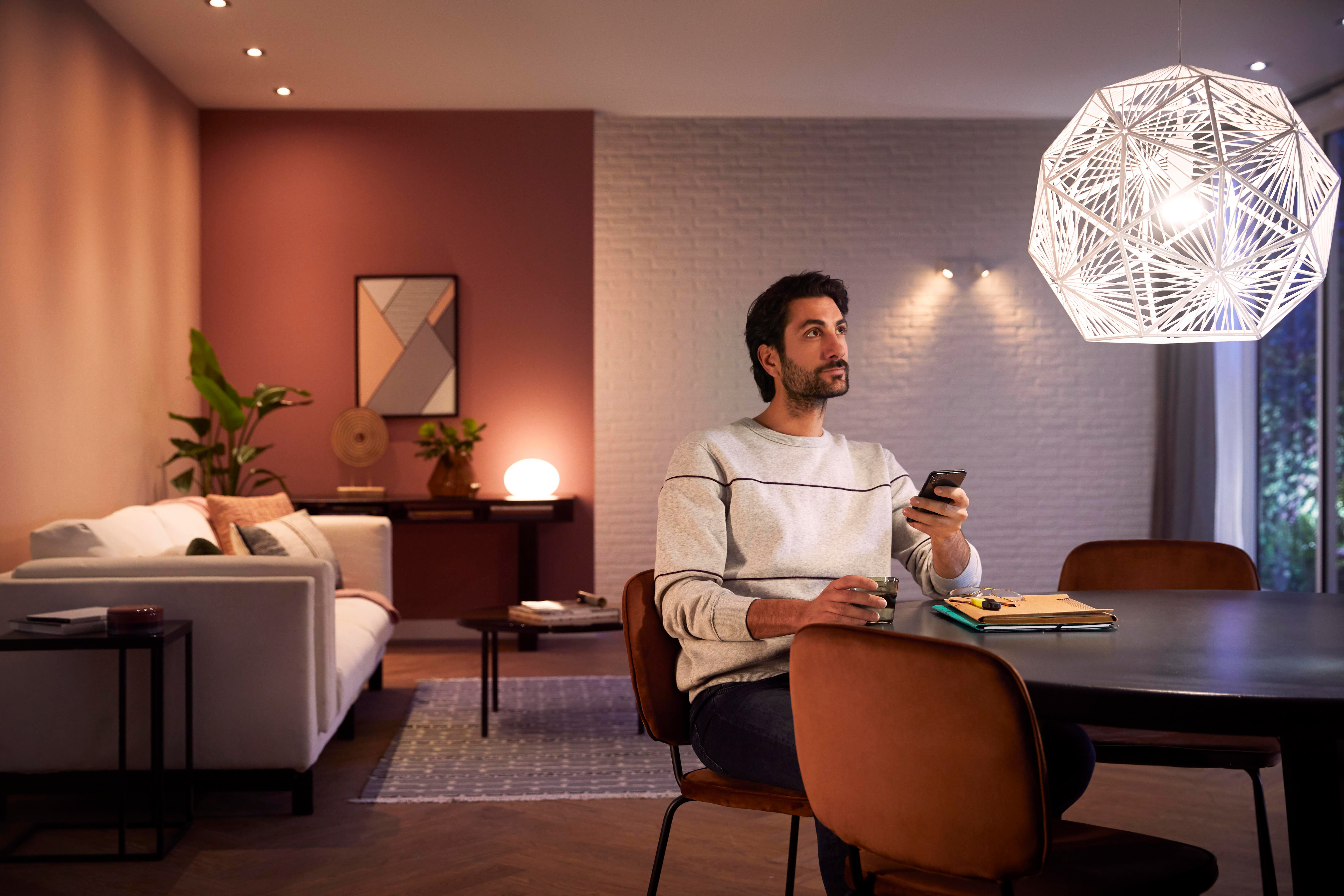 Ein Mann sitzt in einem modernen Wohnzimmer und schaut auf sein Telefon. Eine Pendelleuchte ist oben.