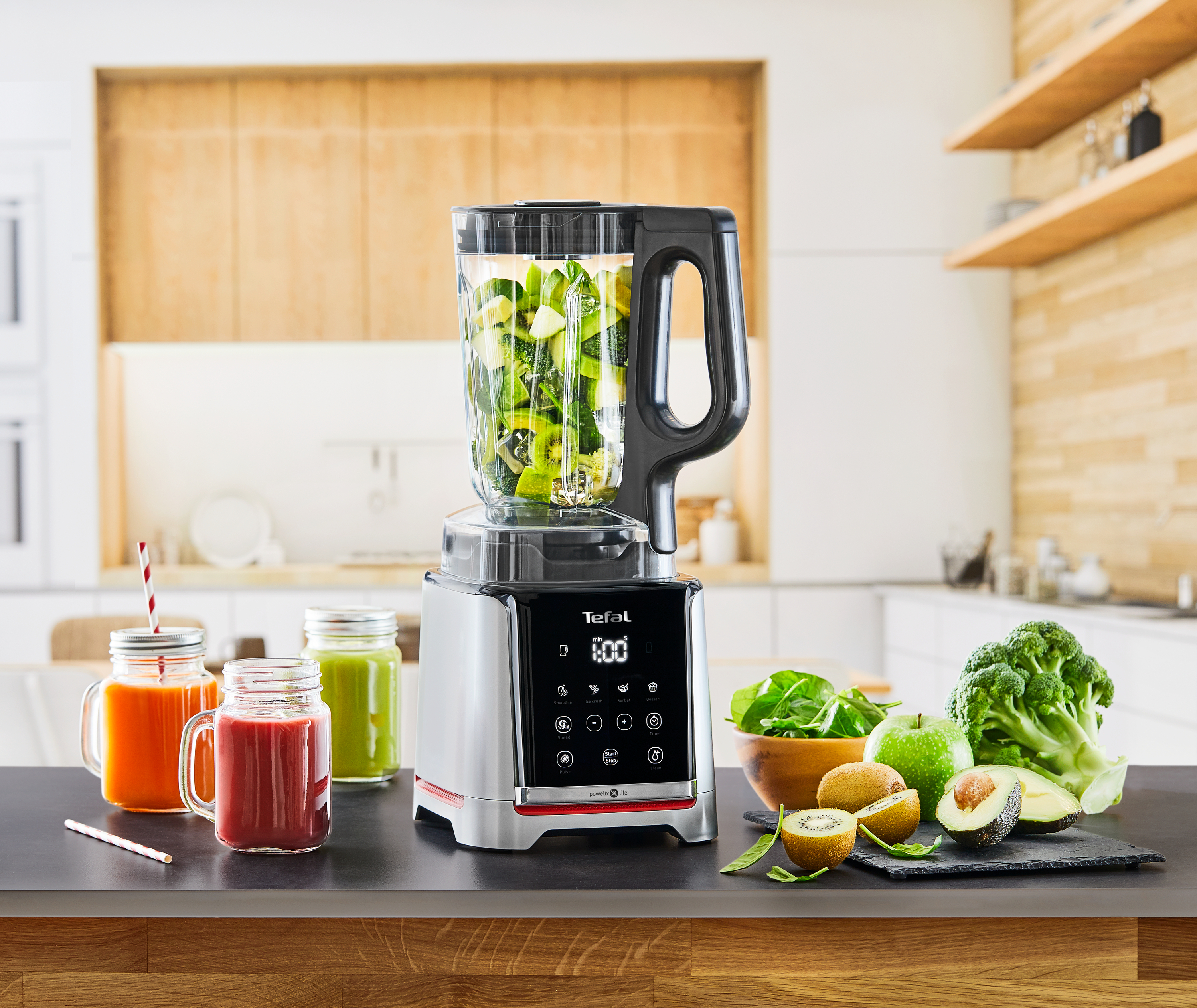 Ein Mixer mit grünen Zutaten, daneben mehrere gläser mit Früchten.