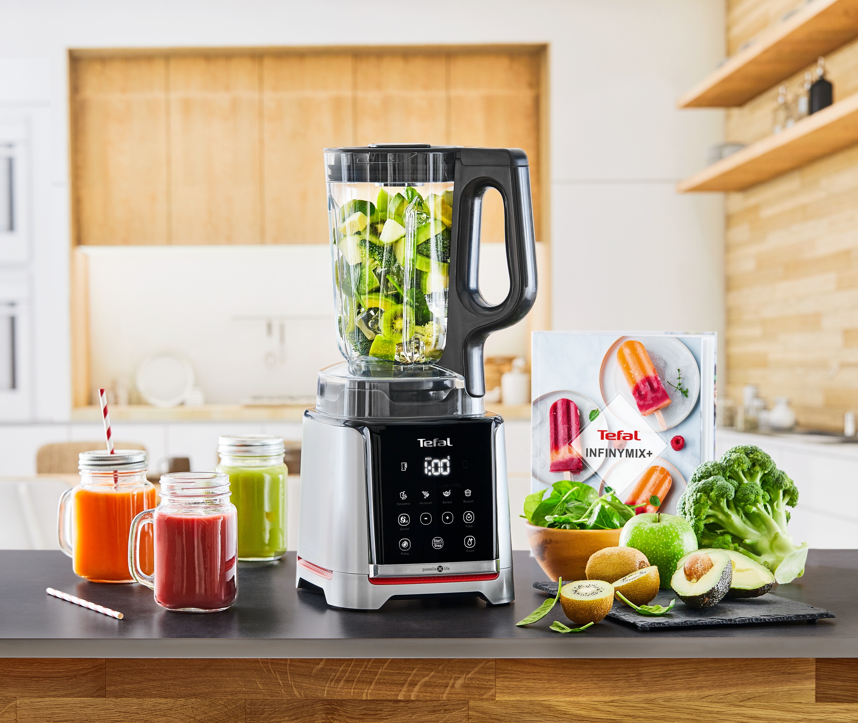 Mixer mit Zutaten. Saftgläser, Früchte und ein Rezeptbuch auf dem Tisch.