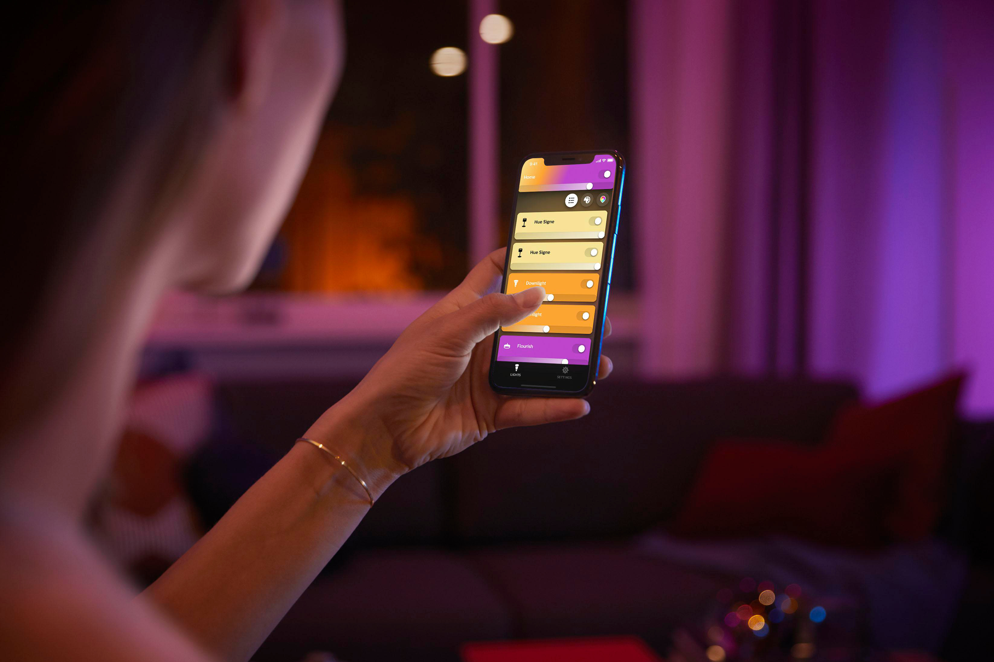 Frau benutzt Telefon, um intelligente Lichter zu steuern. Bunte Lichter und Wohnzimmer im Hintergrund.
