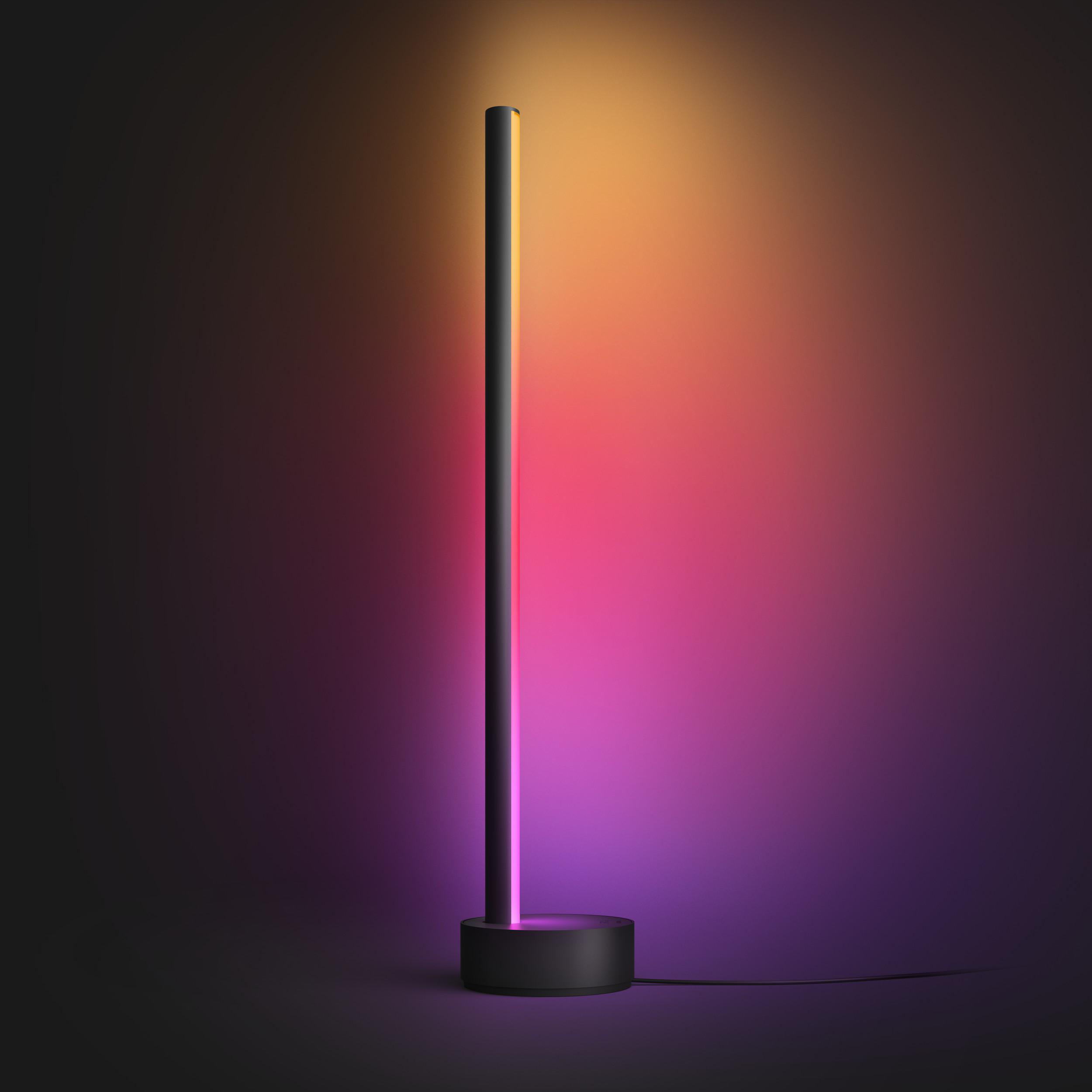 Eine hohe, schwarze, zylindrische Lampe, die mit einem Farbverlauf auf dunklem Hintergrund beleuchtet wird.