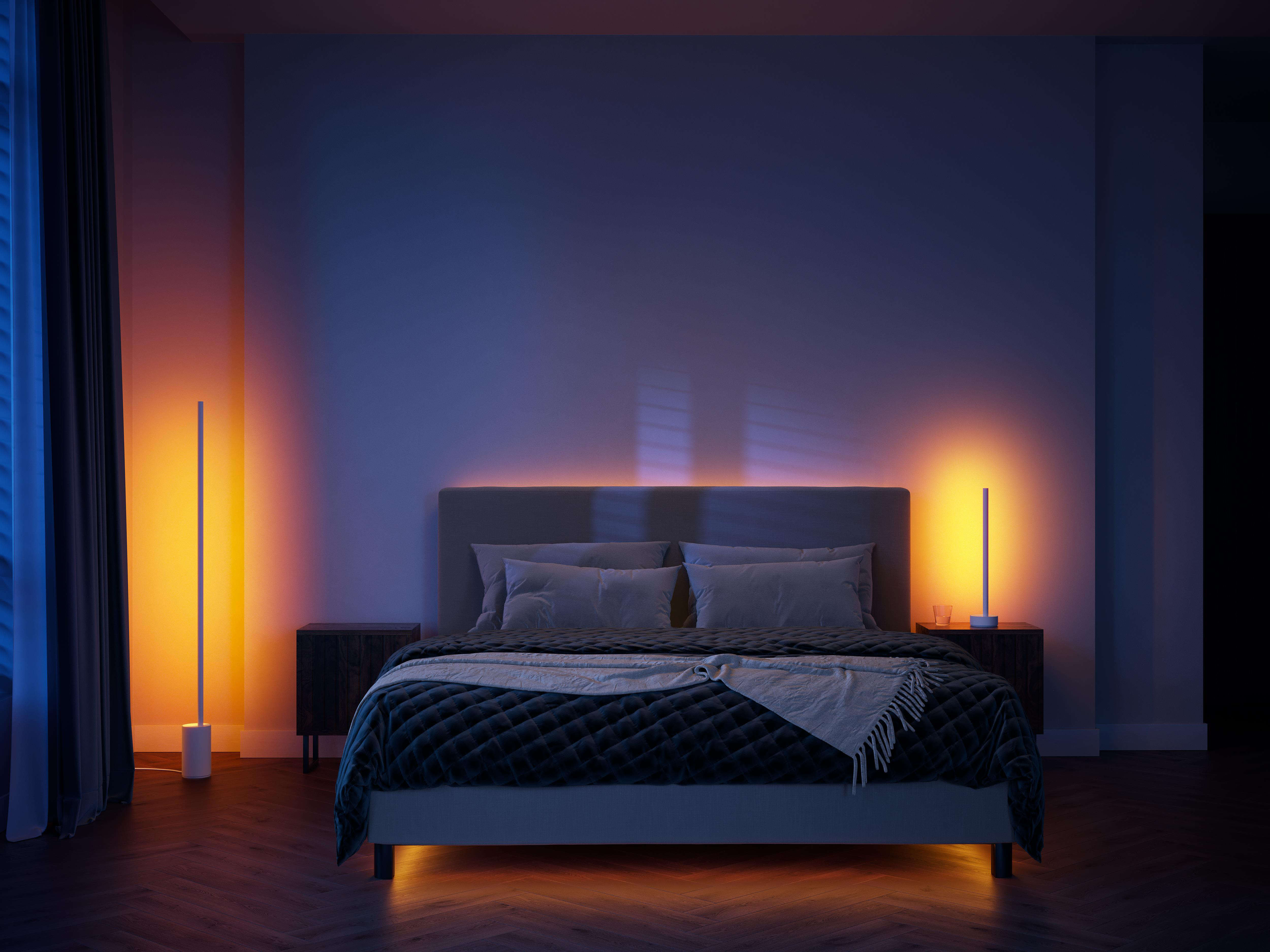 Schlafzimmer mit Bett, Nachttischen und zwei orangefarben beleuchteten Lampen.