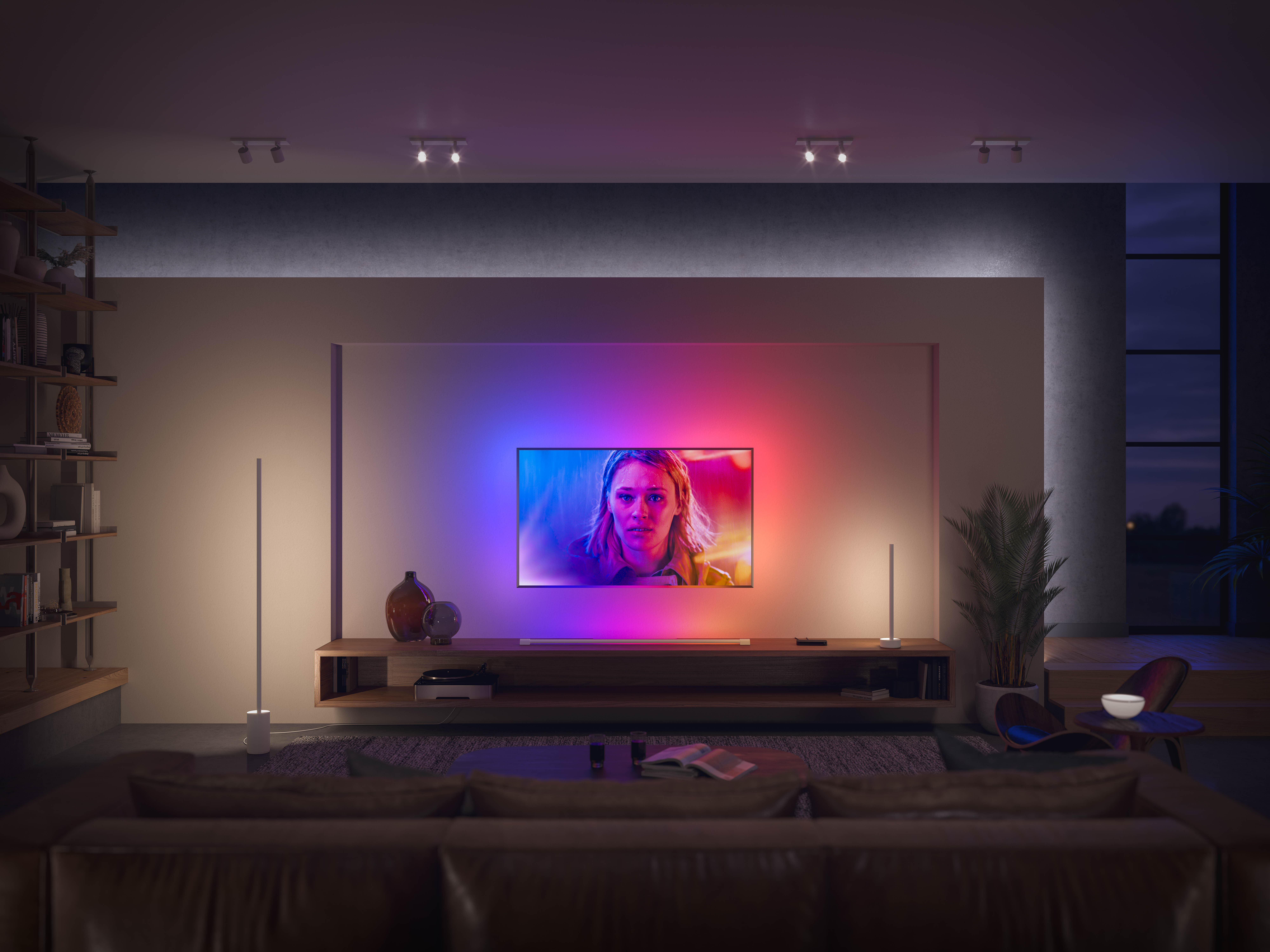 Wohnzimmer mit Fernseher. Der Fernseher ist an, mit einem bunten Bild. Es gibt Lichter und Möbel.