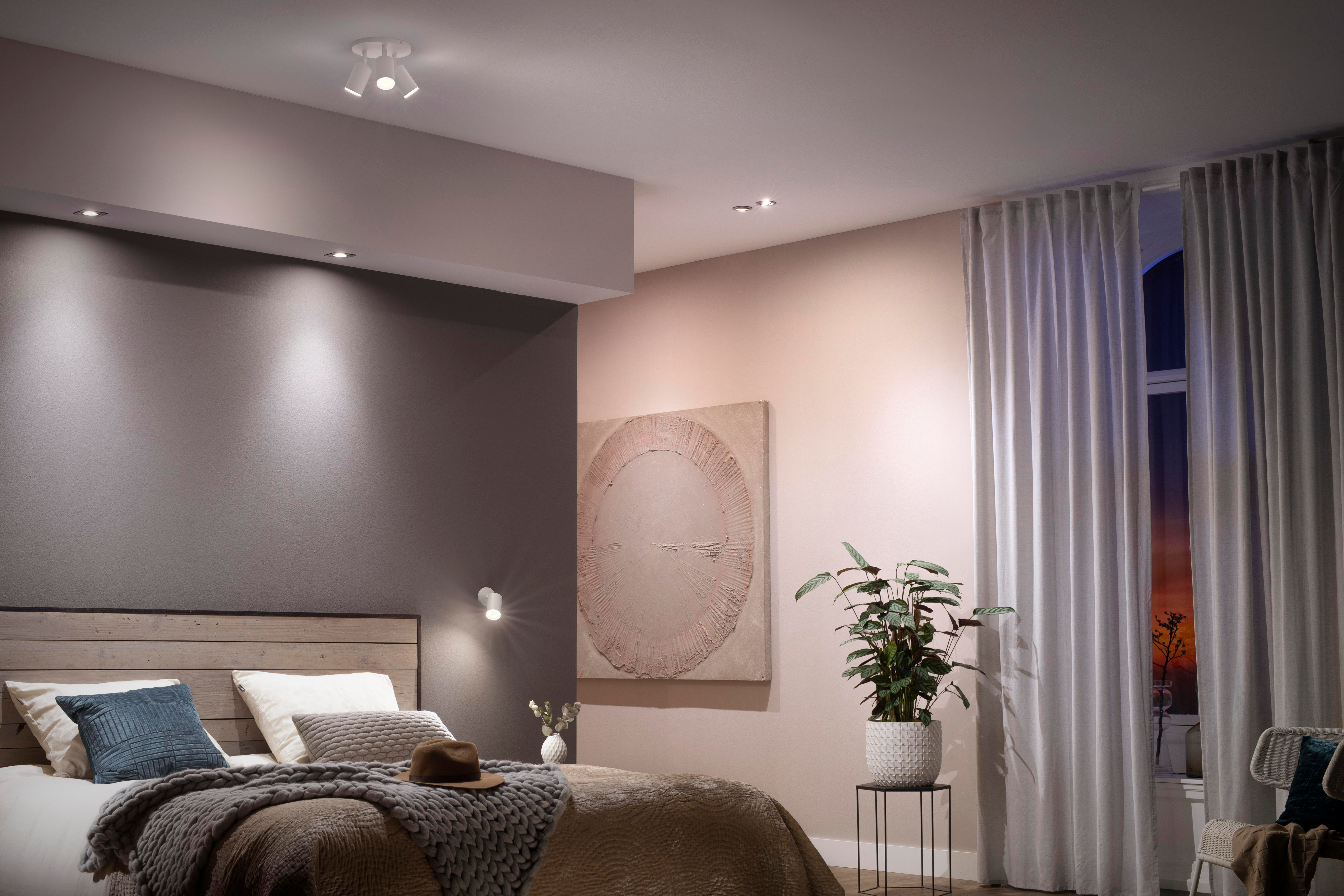 Schlafzimmer mit Bett, Kopfteil, Kunst und mehreren Lichtern an Decke und Wand.