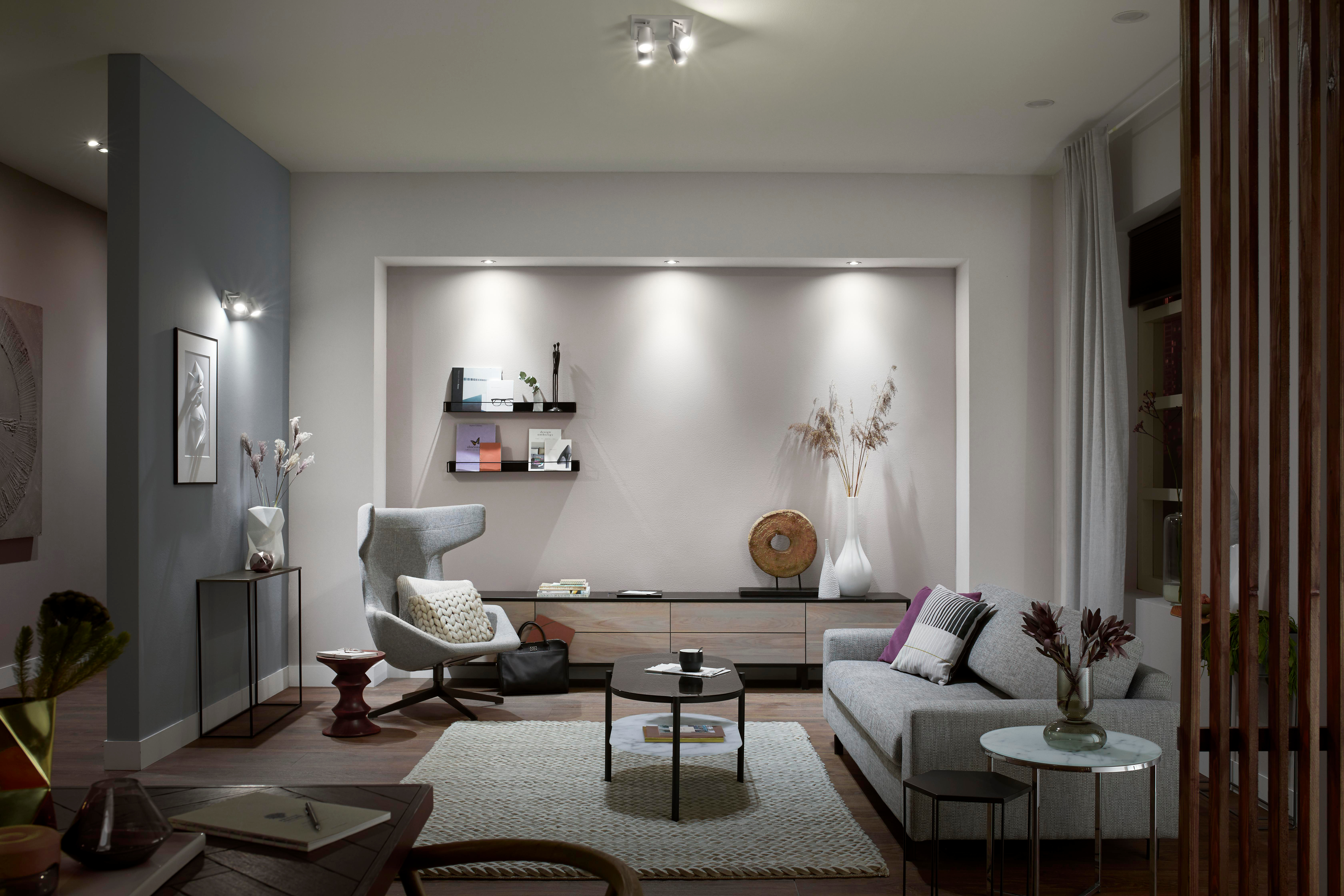 Ein modernes Wohnzimmer mit Couch, Stühlen und einem Couchtisch. Es gibt Lichter an den Wänden.