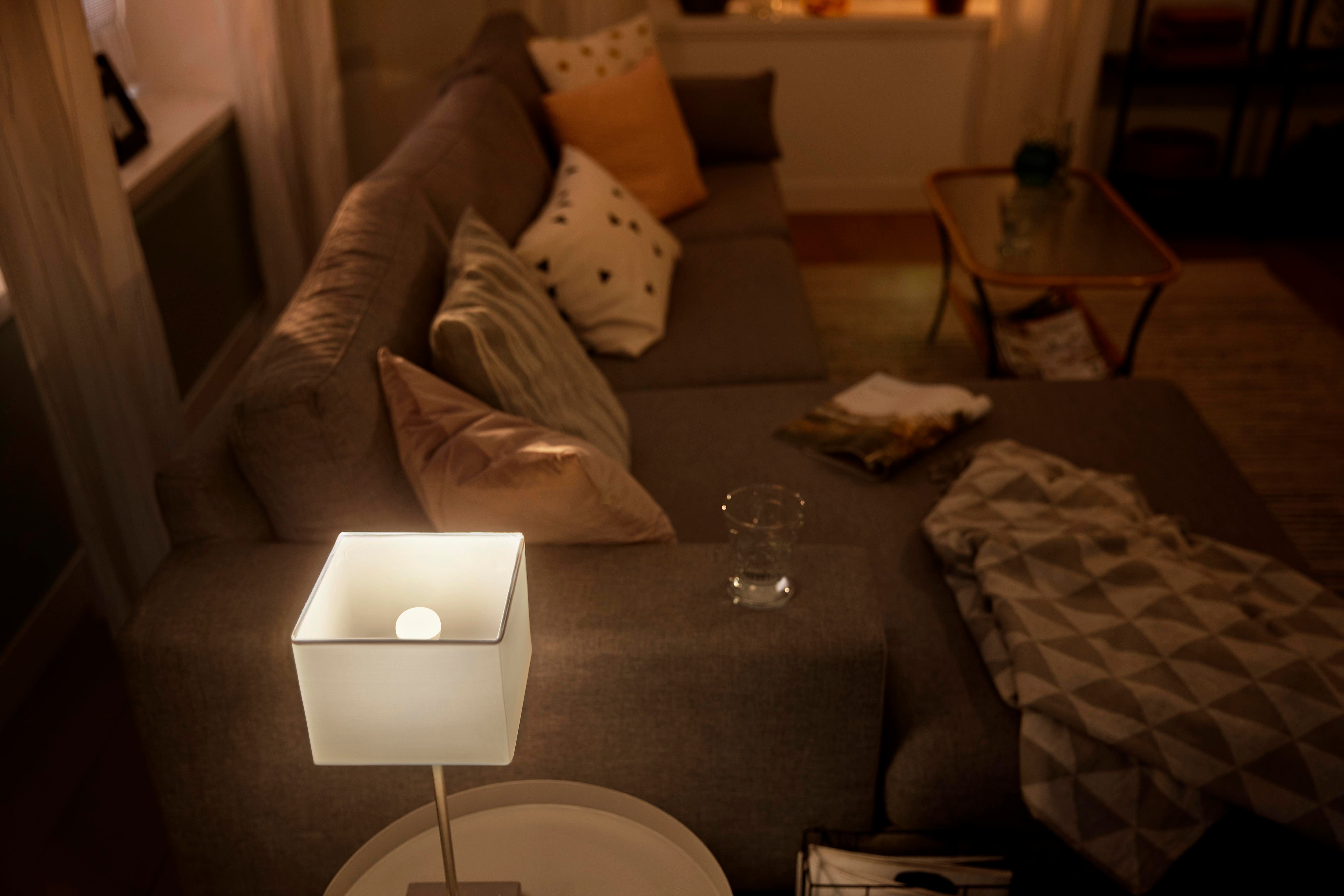 Lampe auf Tisch mit Glas und Decke auf Sofa. Kleines Fenster links.