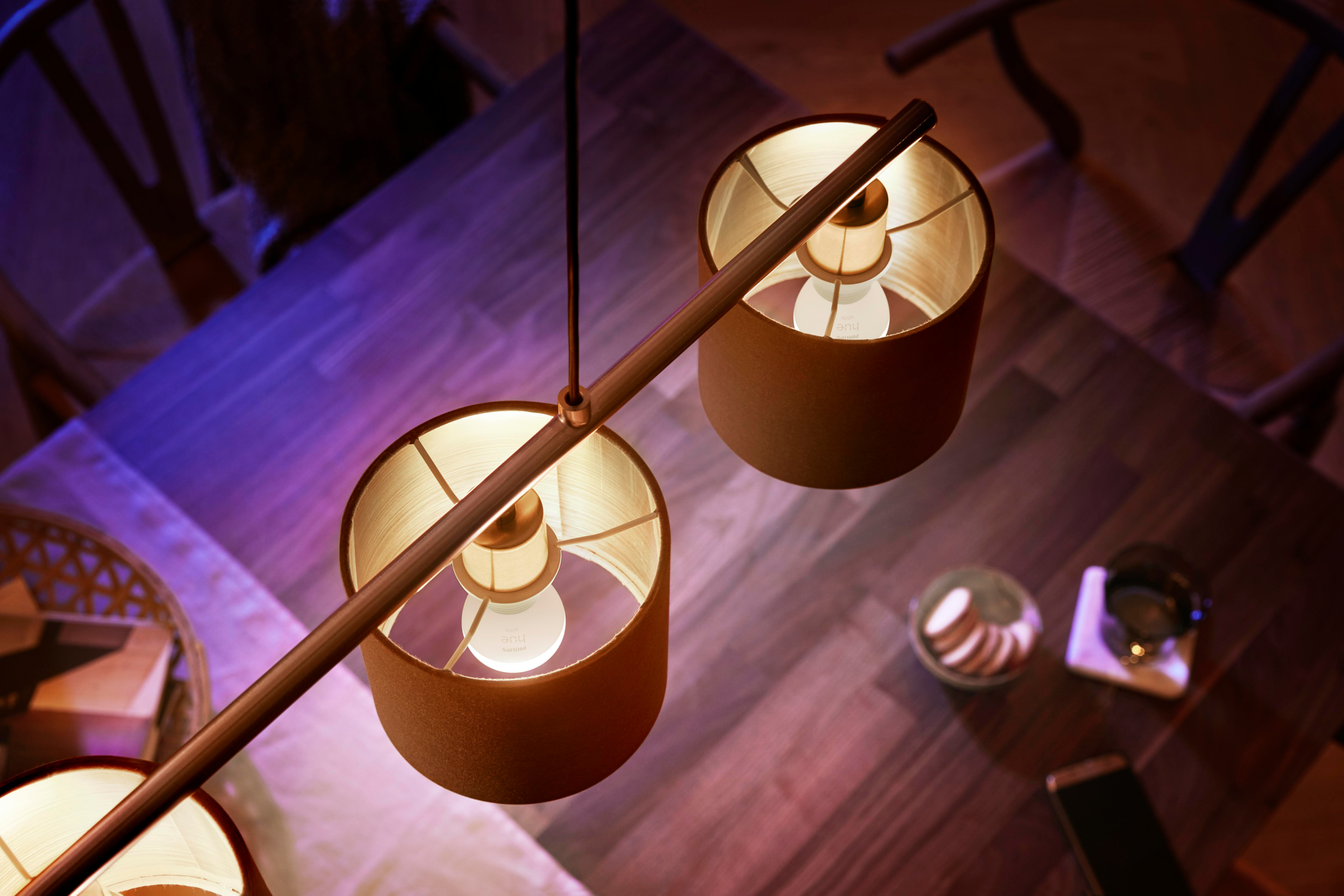 Zwei Lampen mit leuchtenden Glühbirnen, die ein warmes Licht in einem Raum mit Holztisch und Glas zeigen.