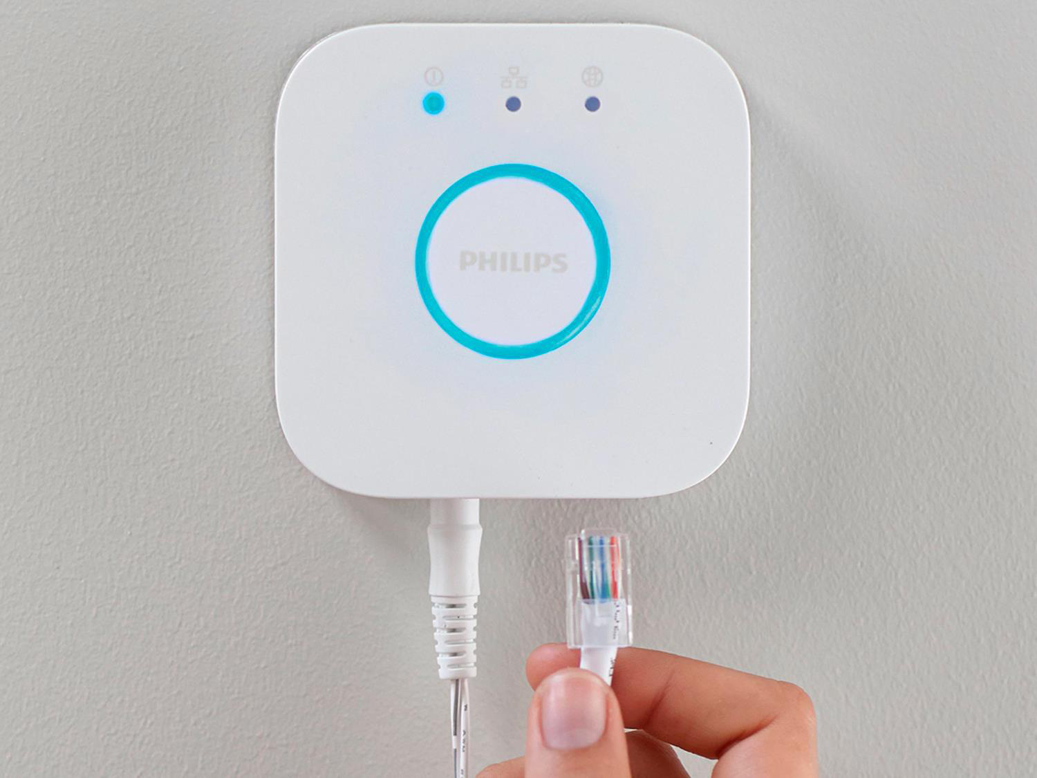Eine weiße Philips Hue Bridge mit eingestecktem Kabel. Eine Hand hält das Kabel.