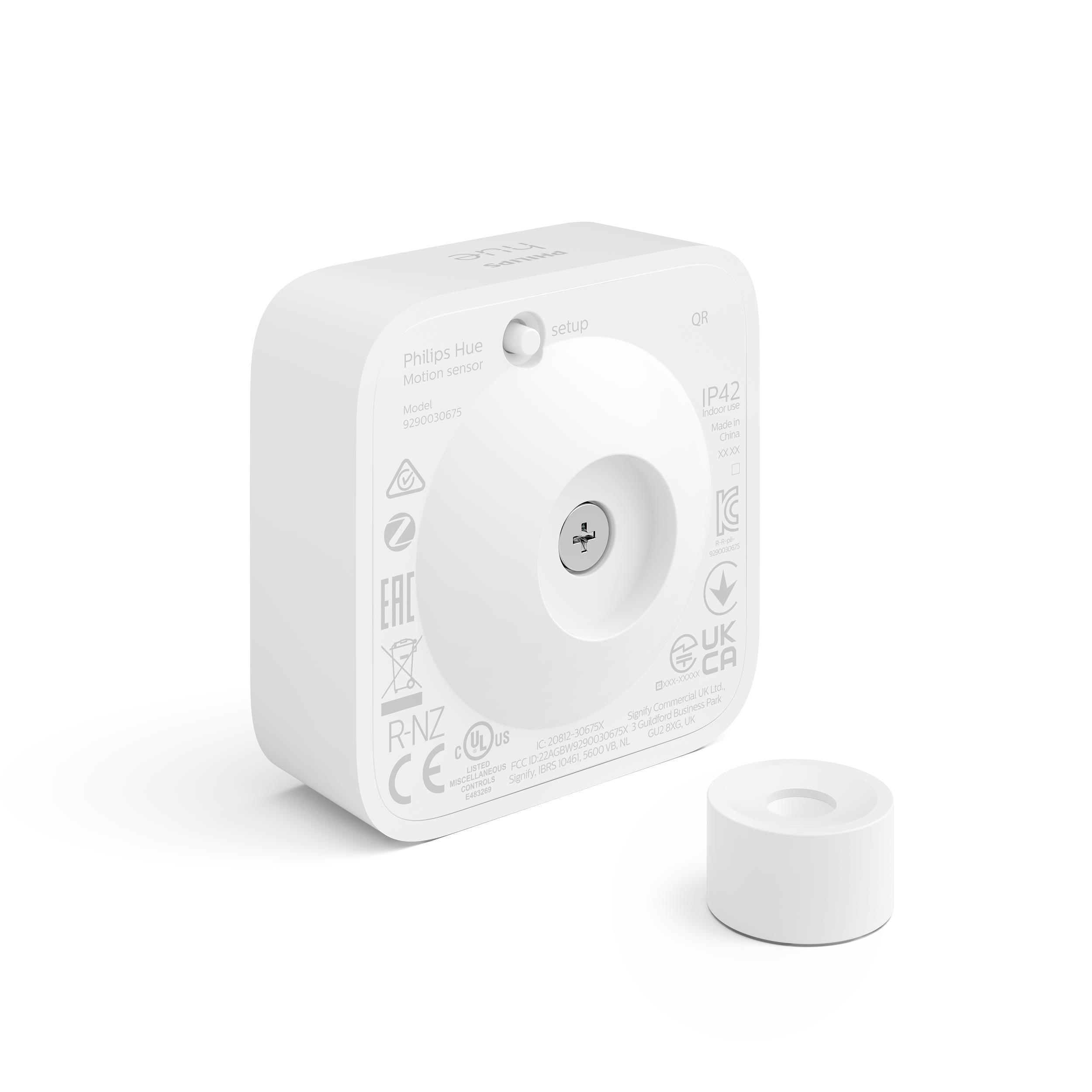 Ein weißer Bewegungssensor mit passendem Sockel. Der Sensor hat ein rundes Objektiv und mehrere Etiketten.