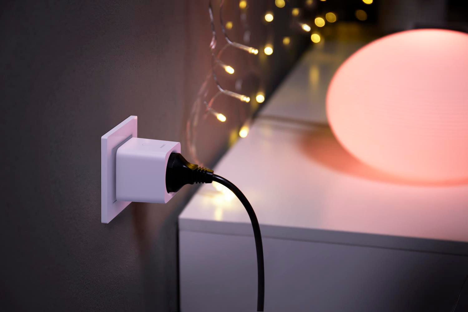 Ein weißer Smart-Stecker ist in eine graue Wand eingesteckt. Ein schwarzes Kabel und eine rosa beleuchtete Lampe sind sichtbar.