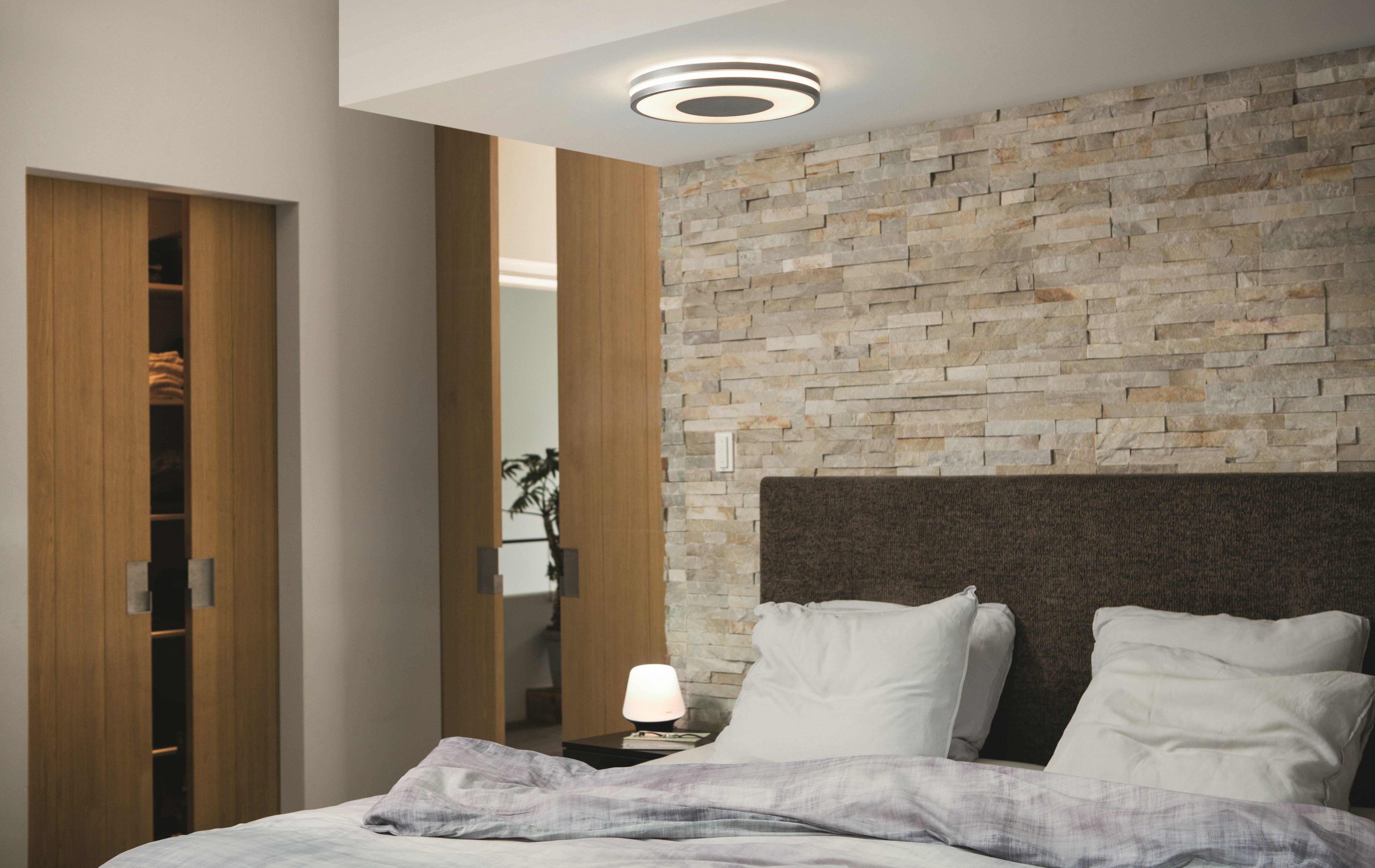 Ein Schlafzimmer mit Bett, Schiebetüren aus Holz und einer Steinmauer. Eine kleine Tischlampe steht auf dem Nachttisch.