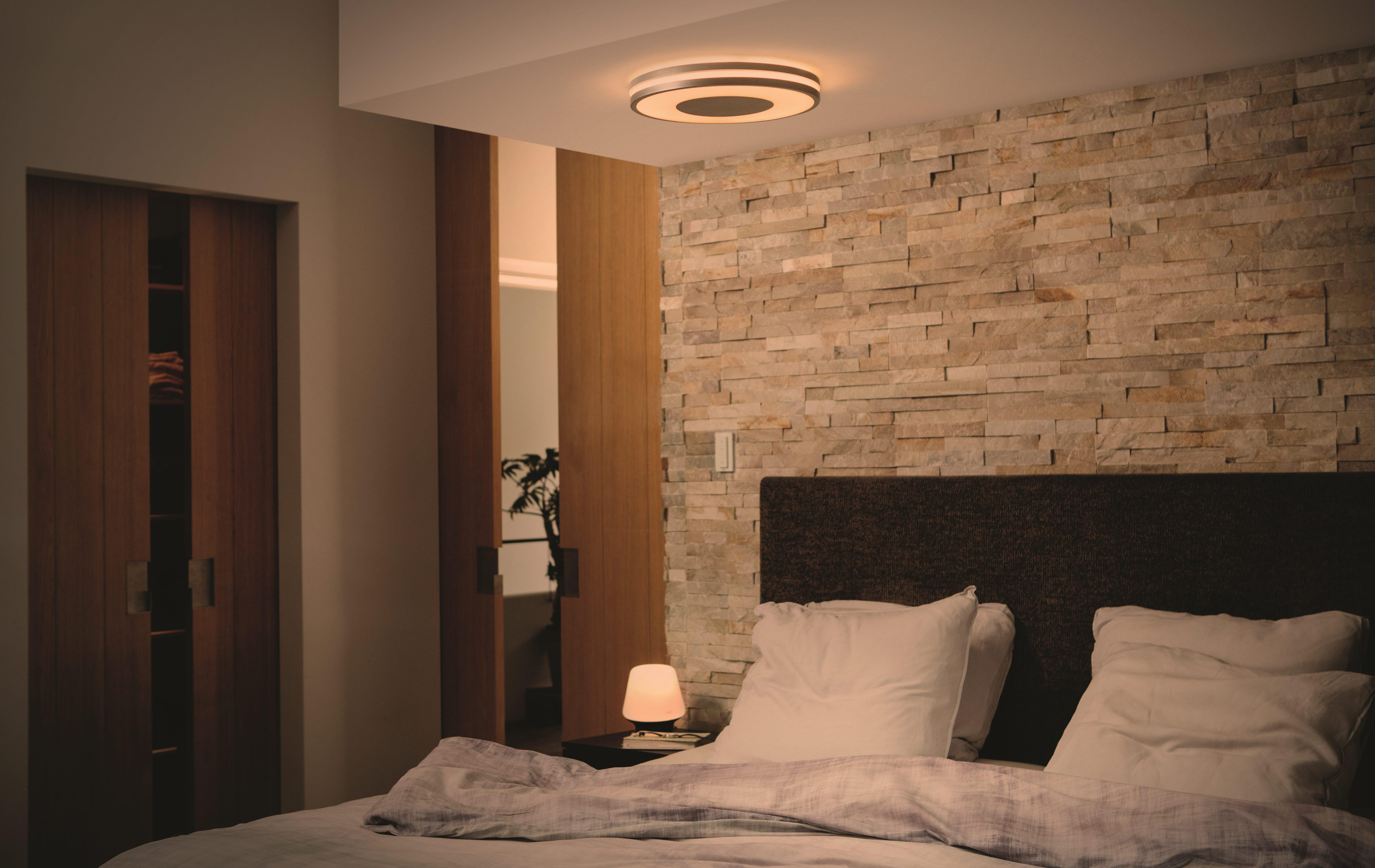 Ein Schlafzimmer mit Bett, Nachttisch mit Lampe und Steinmauer.