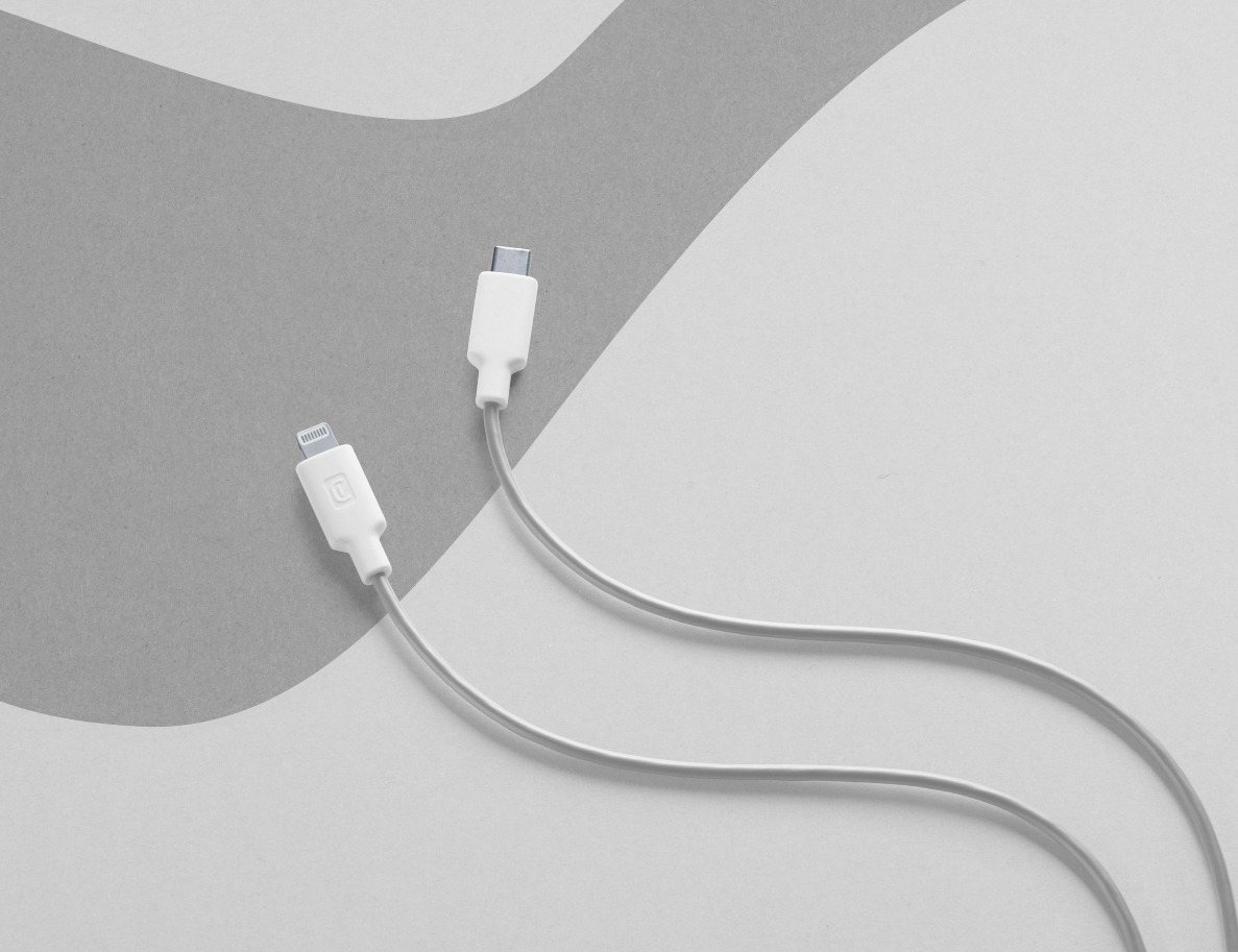 Dos cables de carga blancos con extremos diferentes sobre un fondo gris y blanco.