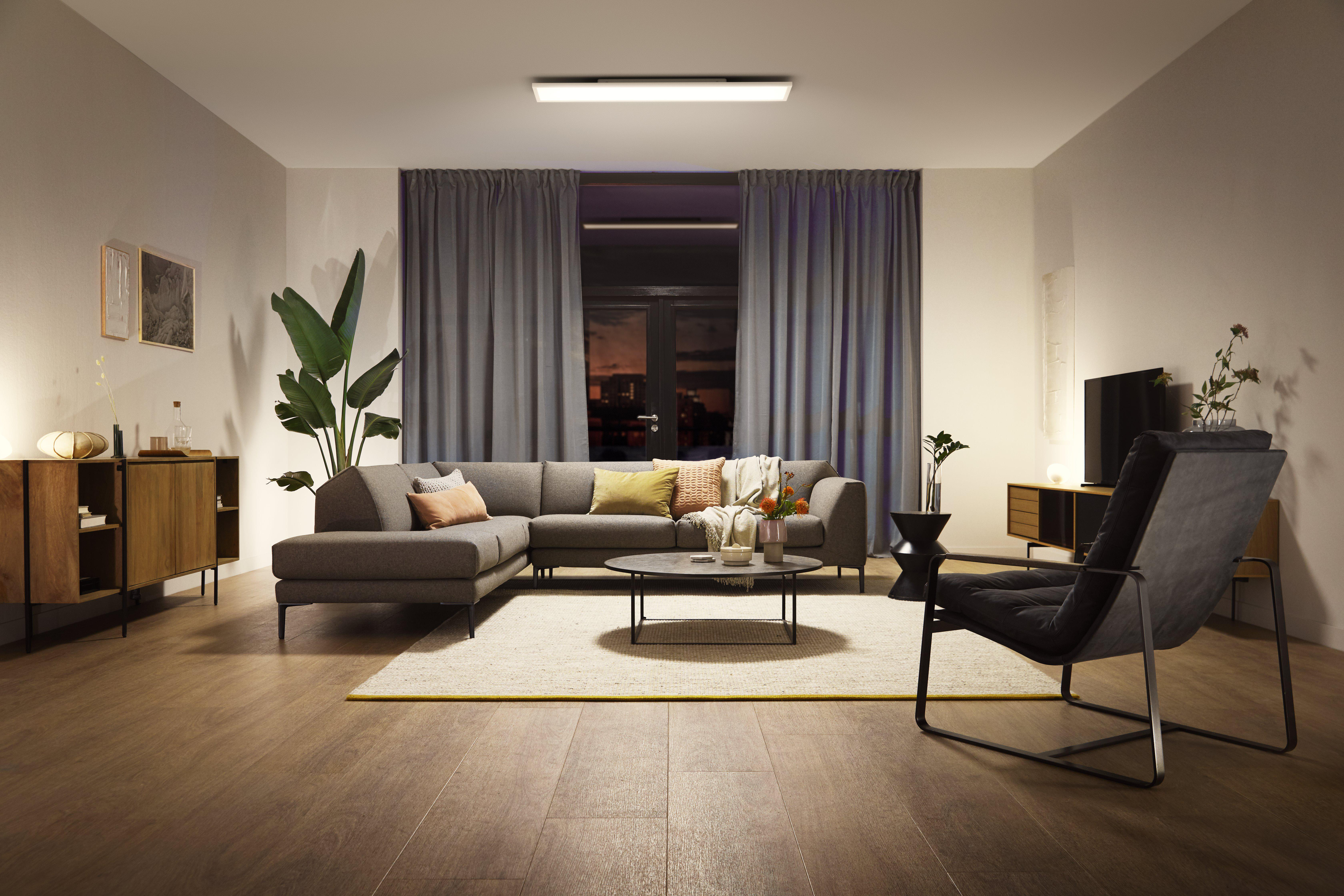 Modernes Wohnzimmer mit grauem Ecksofa, Teppich und großem Fenster mit Vorhängen.