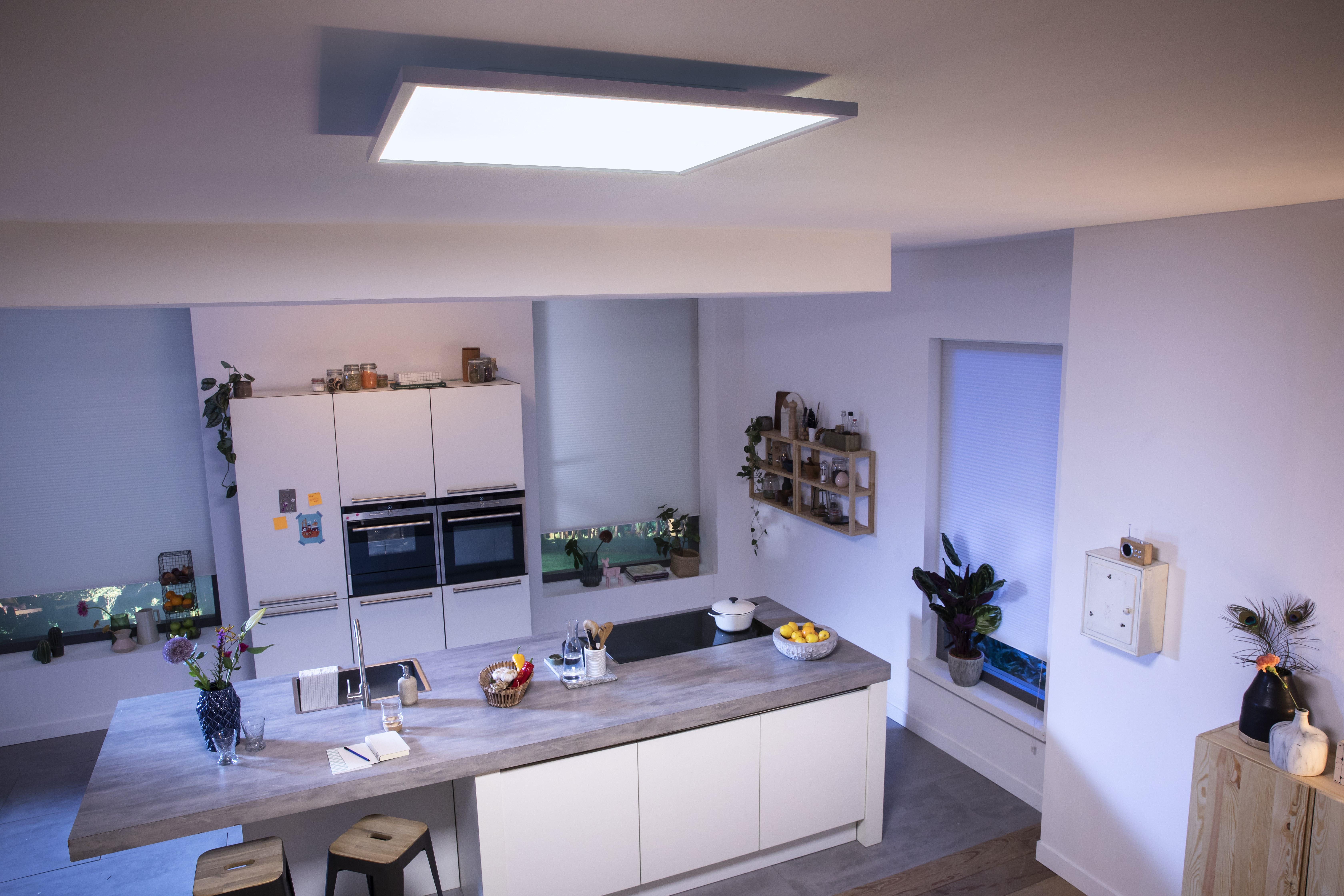 Moderne Küche mit großer Insel. Eine Deckenleuchte befindet sich darüber. Sonnenlicht scheint durch die Fenster.