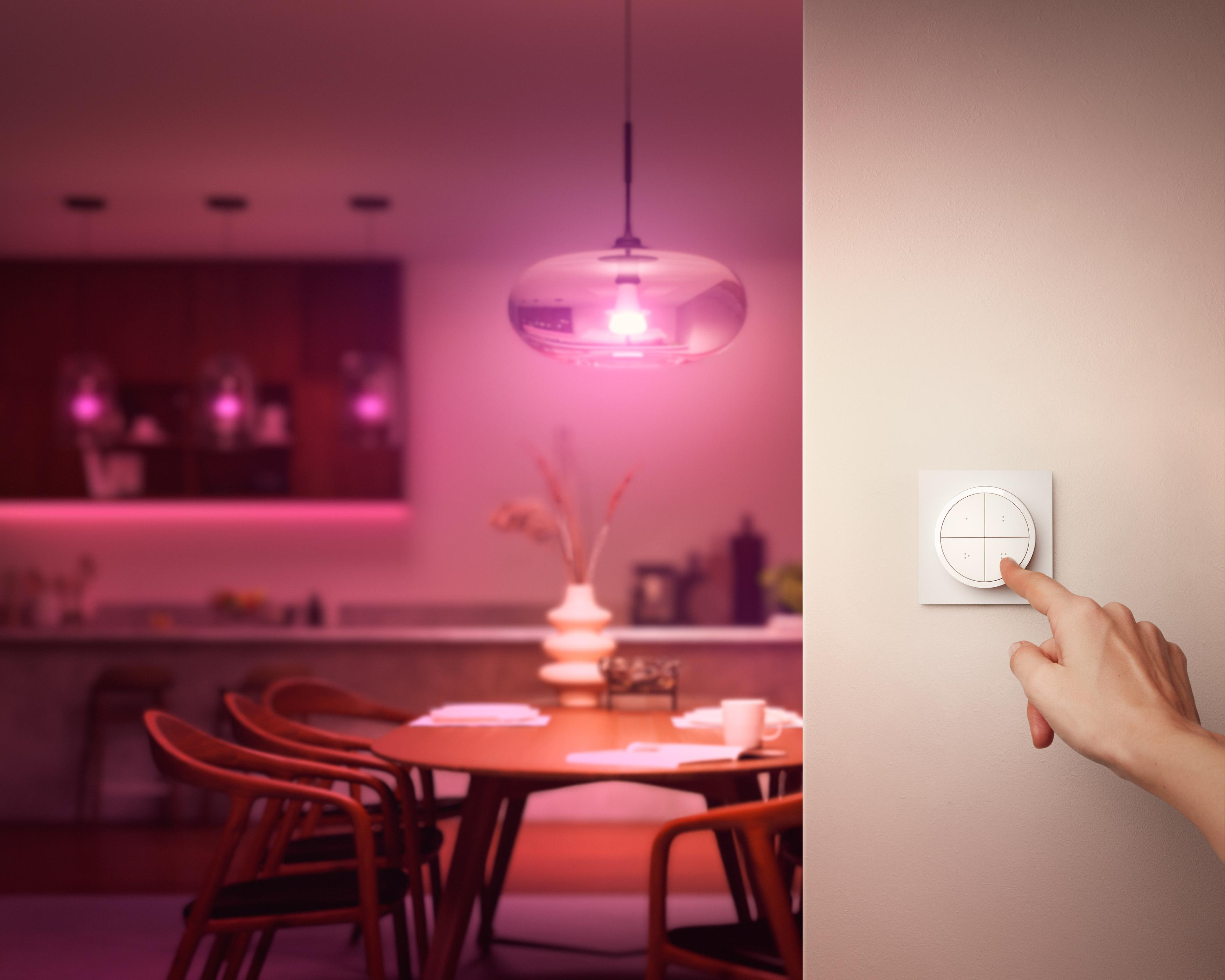 Eine Hand bedient einen Lichtschalter an der Wand, im Hintergrund ein beleuchteter Raum.