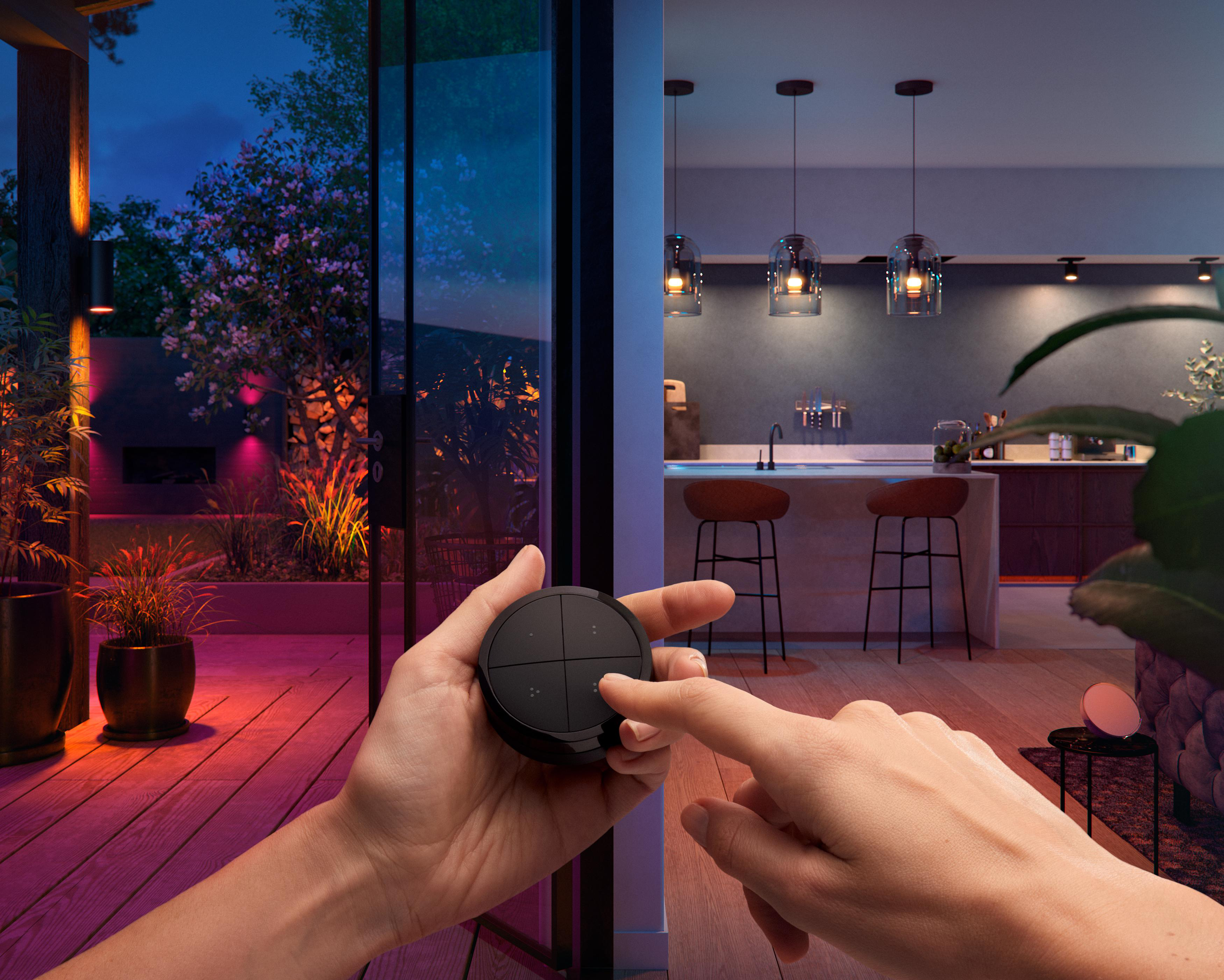 Hände halten eine Philips Hue Fernbedienung, mit Blick auf einen beleuchteten Außenbereich.