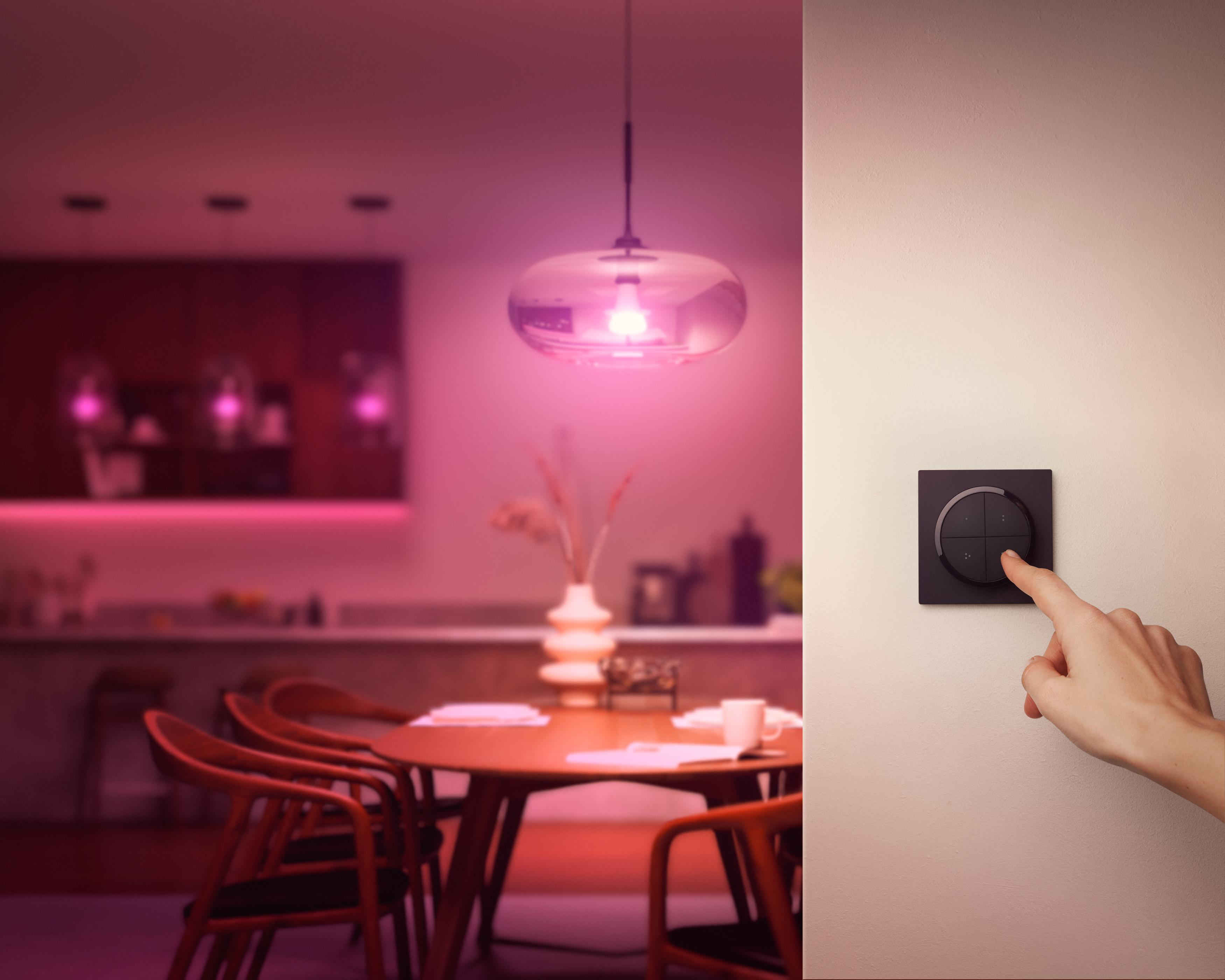 Hand drückt Wandschalter. Essbereich im Hintergrund mit Licht.