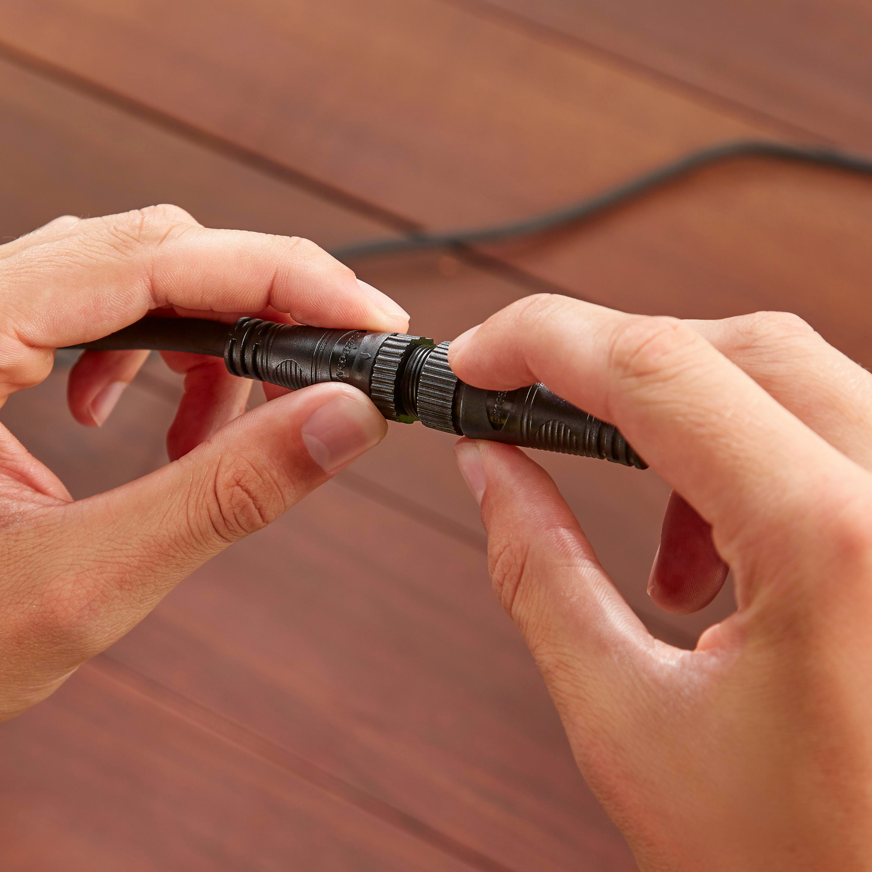 Hände verbinden einen schwarzen Stecker mit einem Kabel auf Holzoberfläche.