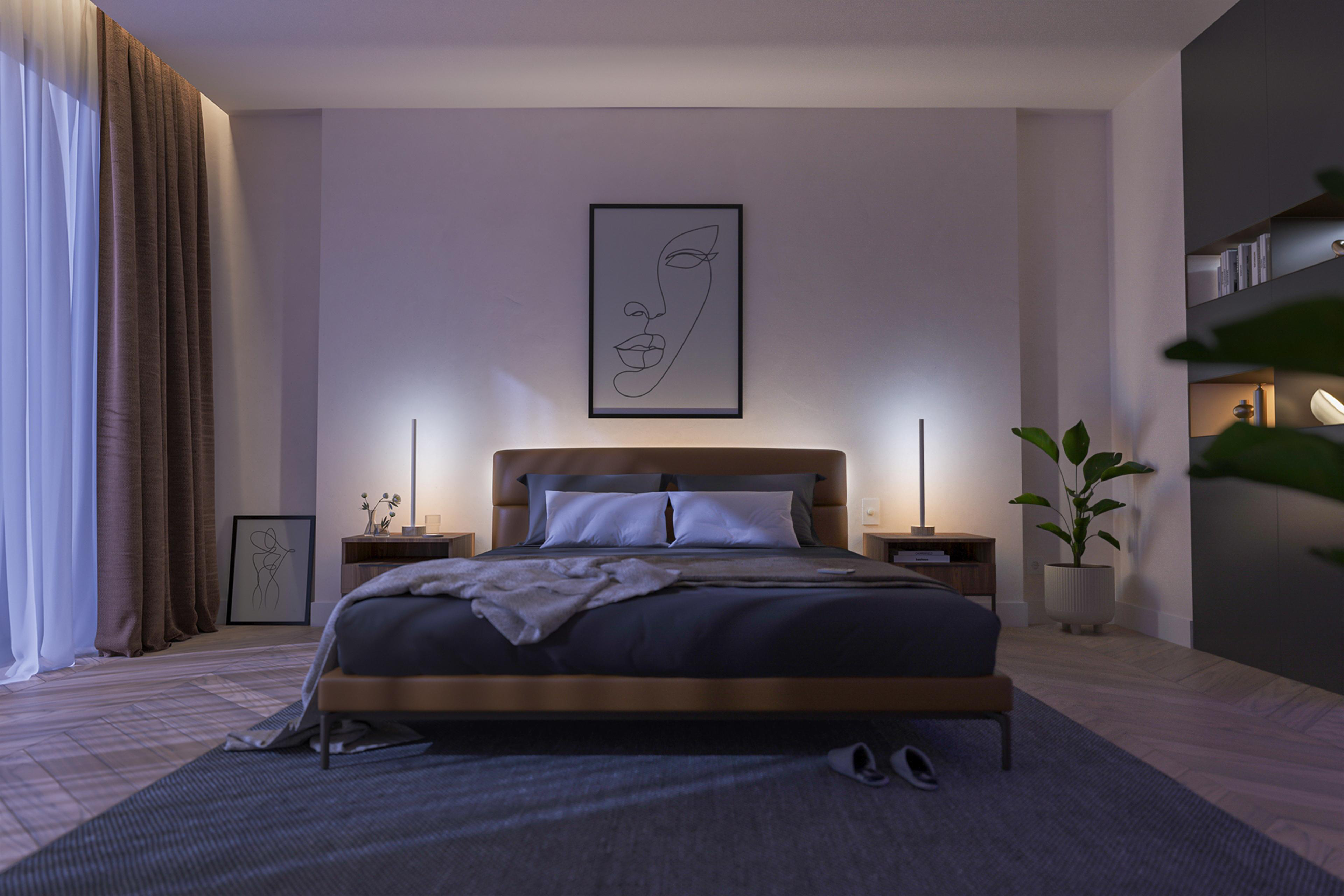 Schlafzimmer mit Bett, zwei Nachttischen mit Lampen und einem Bild an der Wand. Eine Pflanze ist vorhanden.