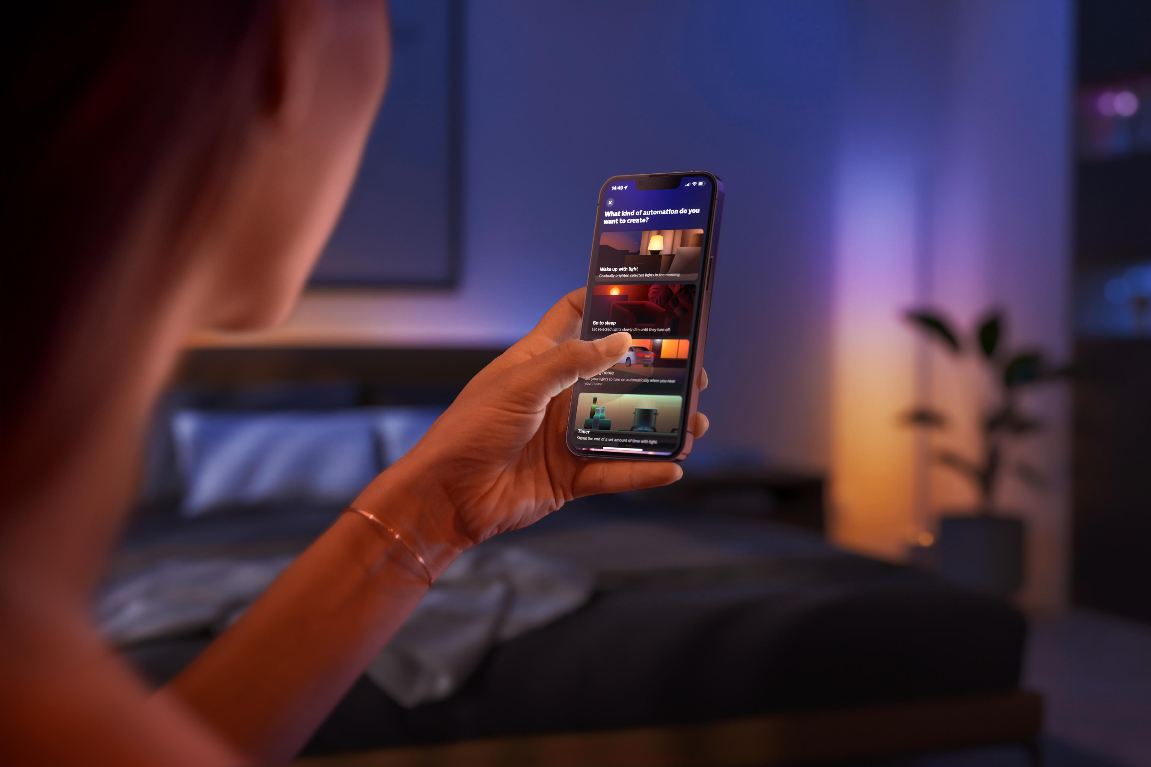 Eine Person hält ein Smartphone mit der Philips Hue App in einem Schlafzimmer.