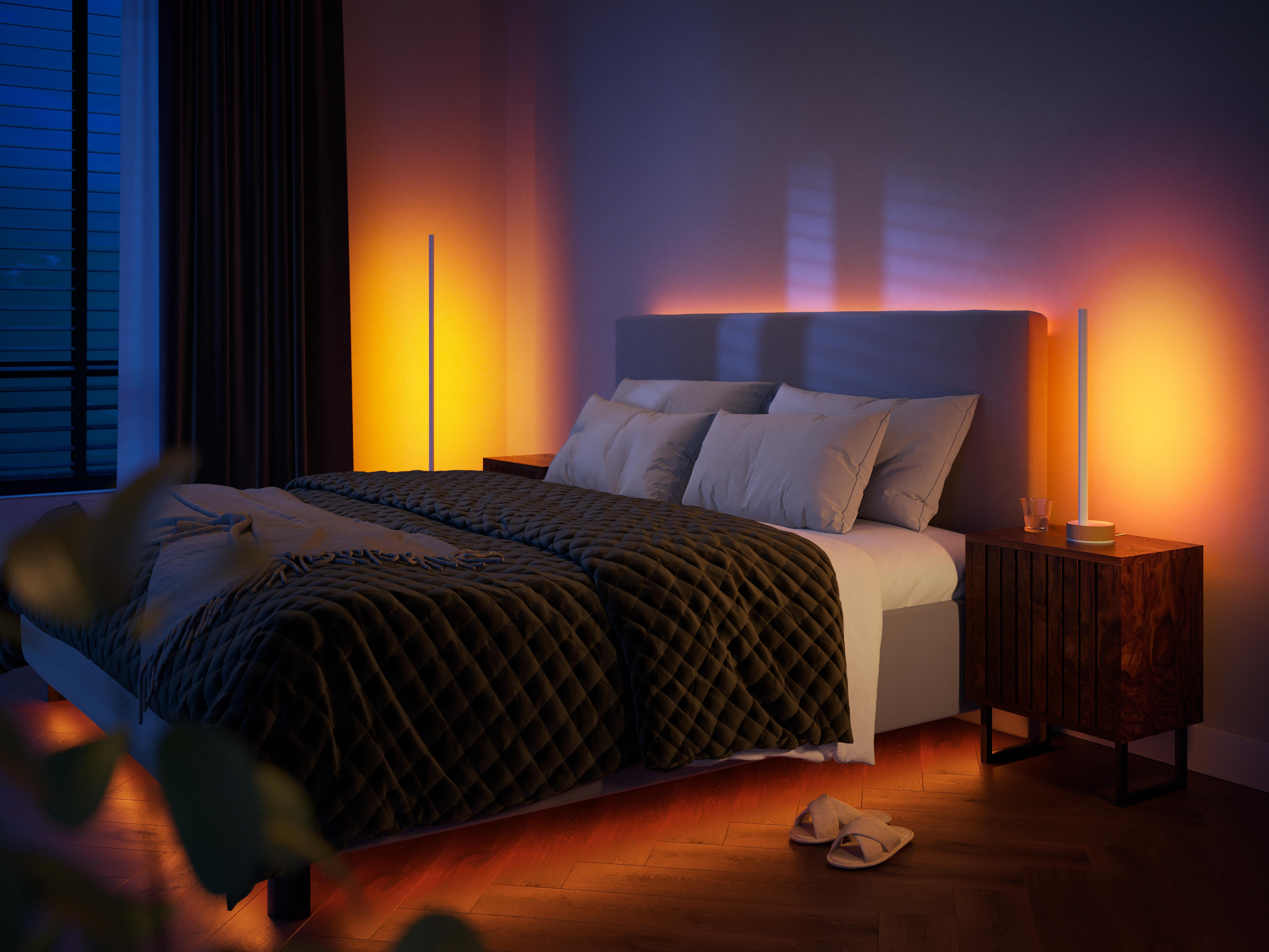 Schlafzimmer mit Bett, Nachttisch mit Lampe und einem Paar Hausschuhen auf dem Boden.