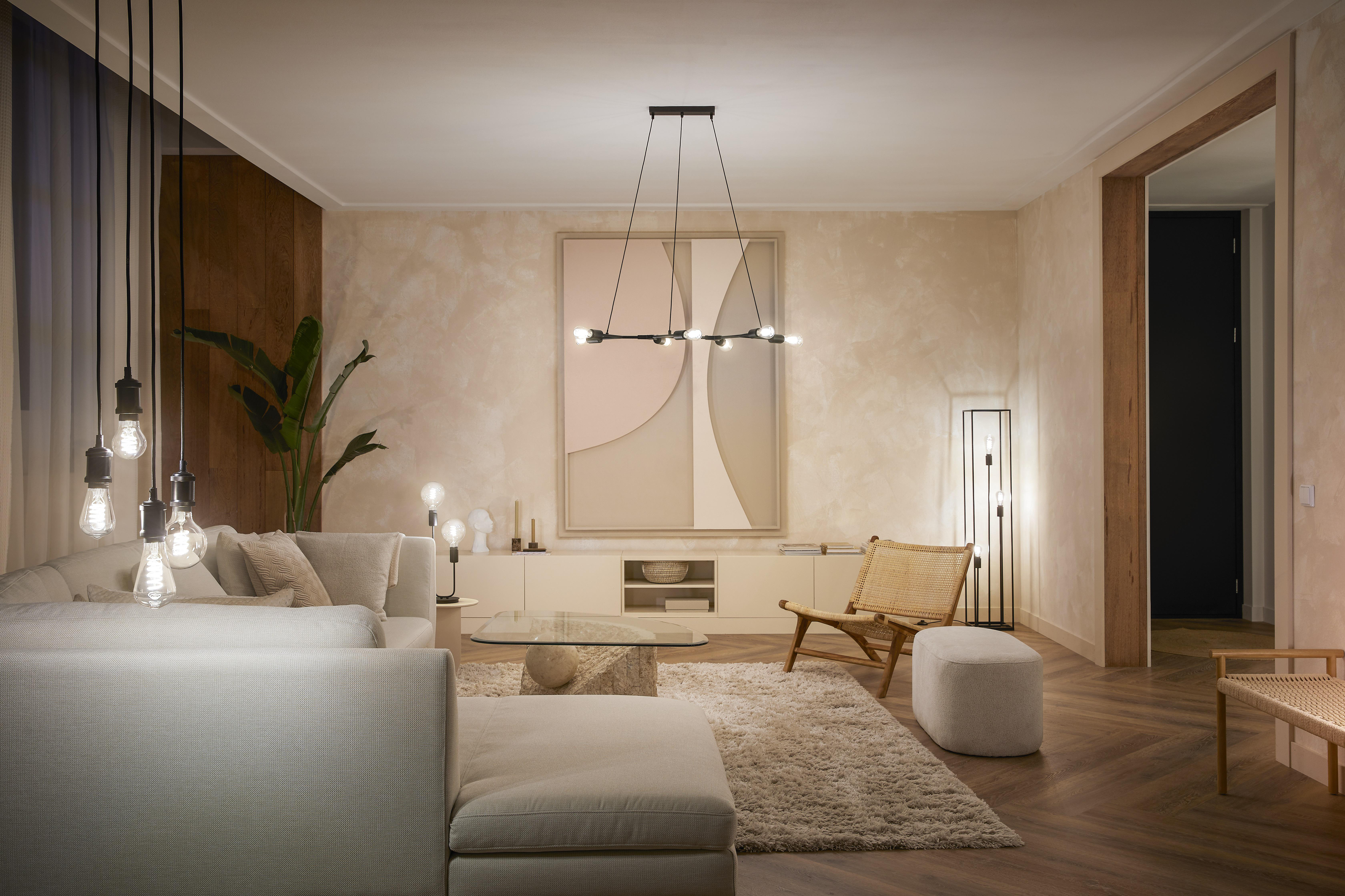 Modernes Wohnzimmer mit Sofa, Teppich, Stuhl und Kunst. Deckenleuchten hängen von der Decke.