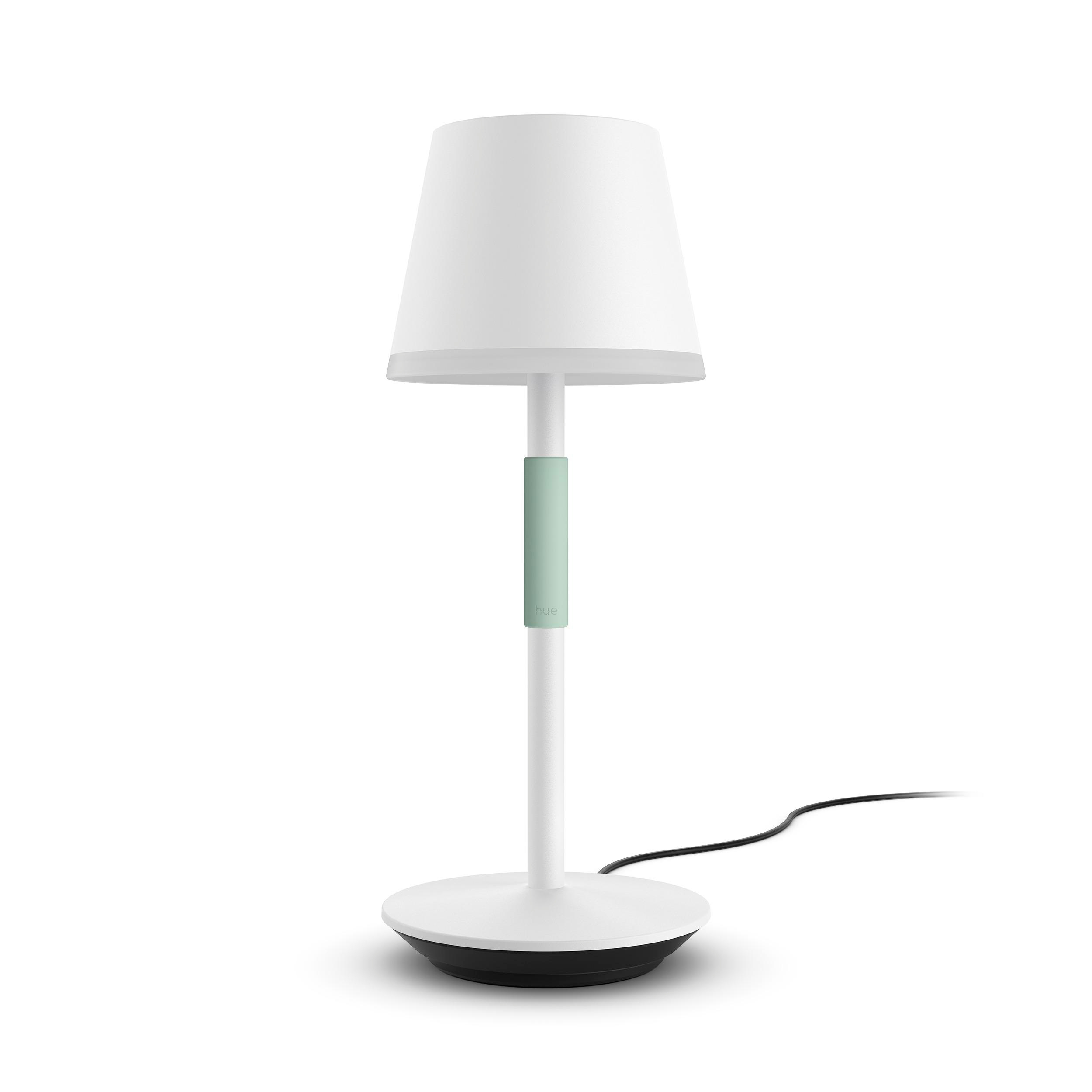 Eine weiße Tischlampe mit grünem Akzent am Stiel und weißem Lampenschirm. Das Kabel ist sichtbar.