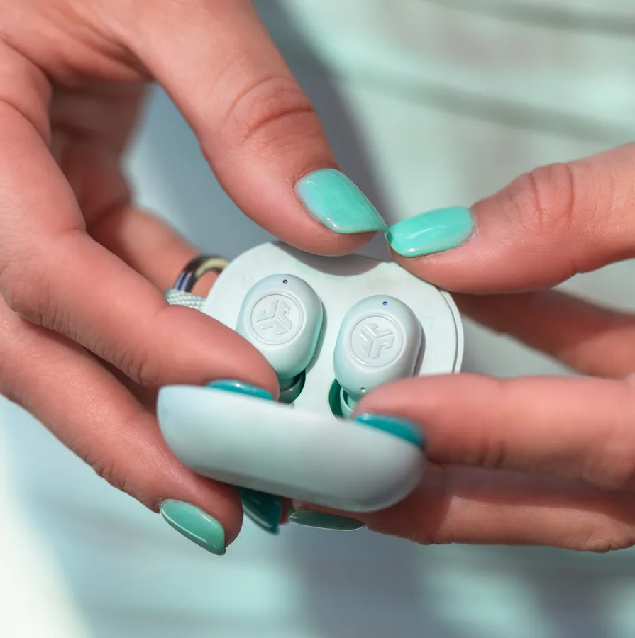Mains tenant un étui de chargement blanc avec écouteurs, montrant des ongles vert menthe.