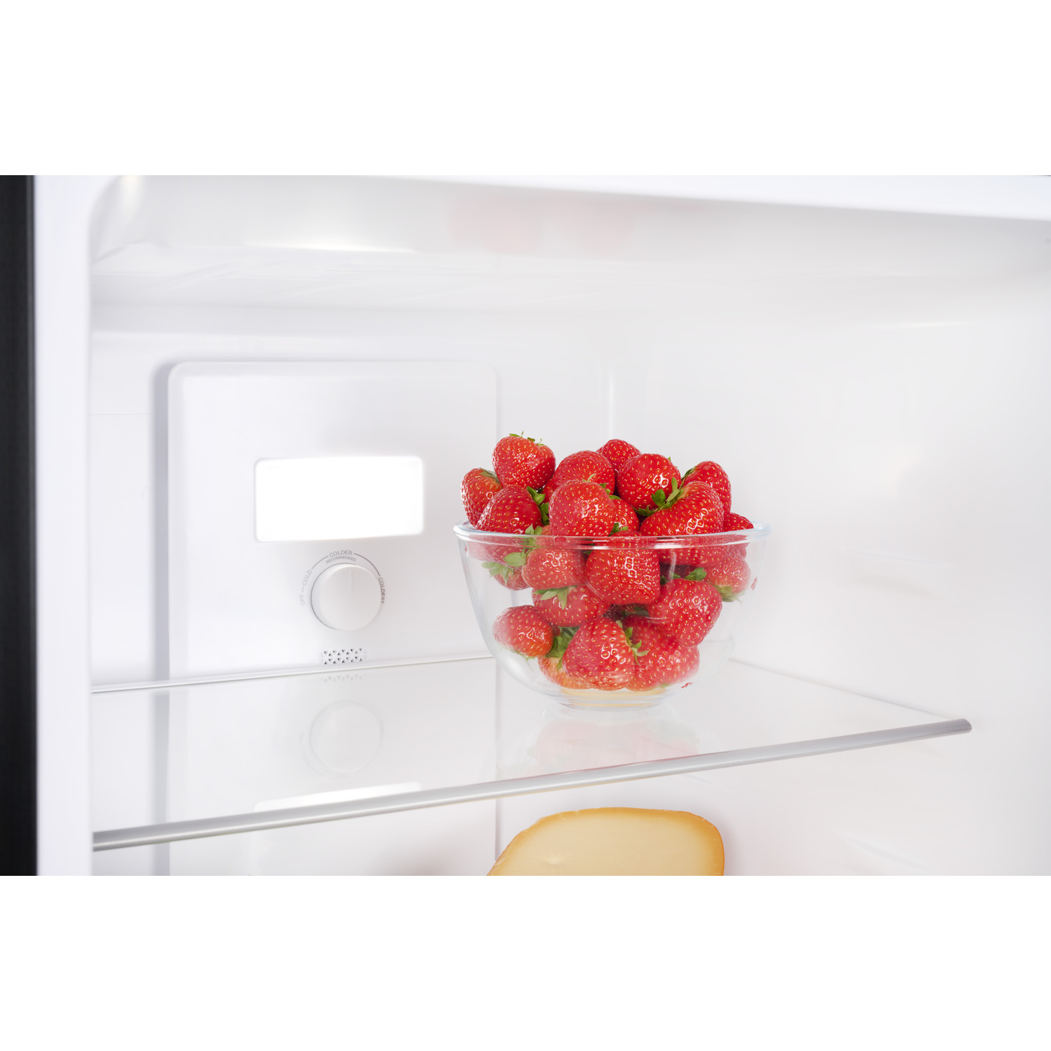 A glass bowl filled with strawberries sits in the refrigerator.