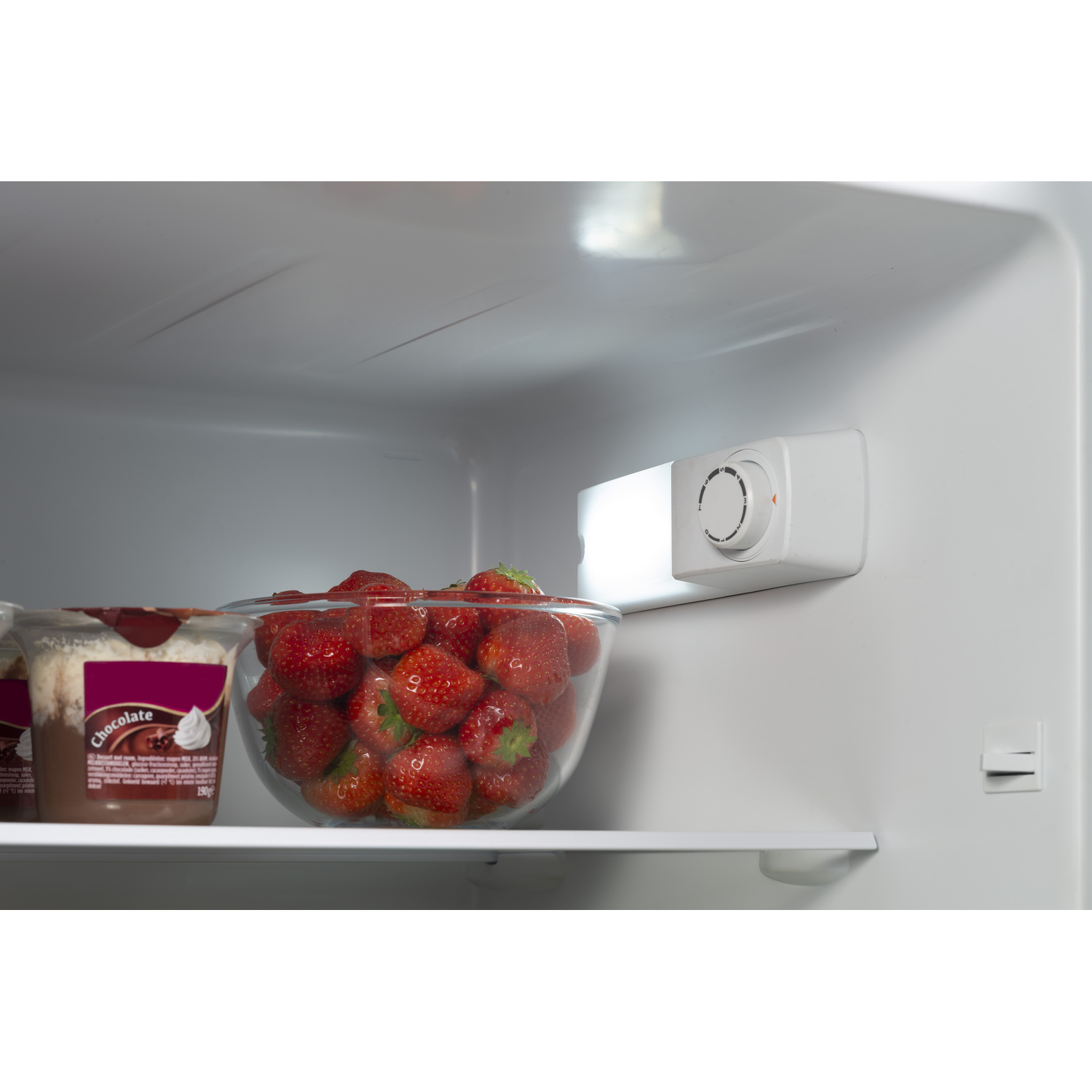 Inside a fridge, a glass bowl of strawberries and a container.